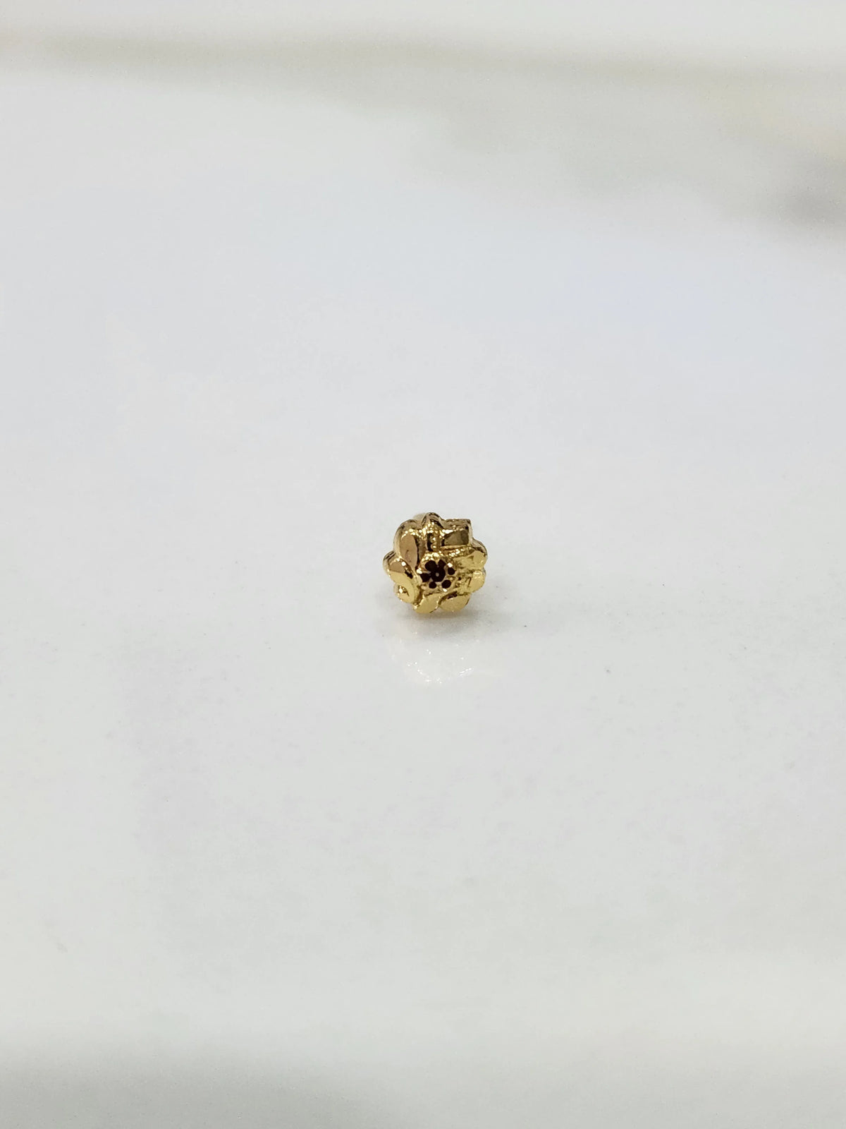 Side view of a delicate gold nose pin on a white surface highlighting fine detailing and shape