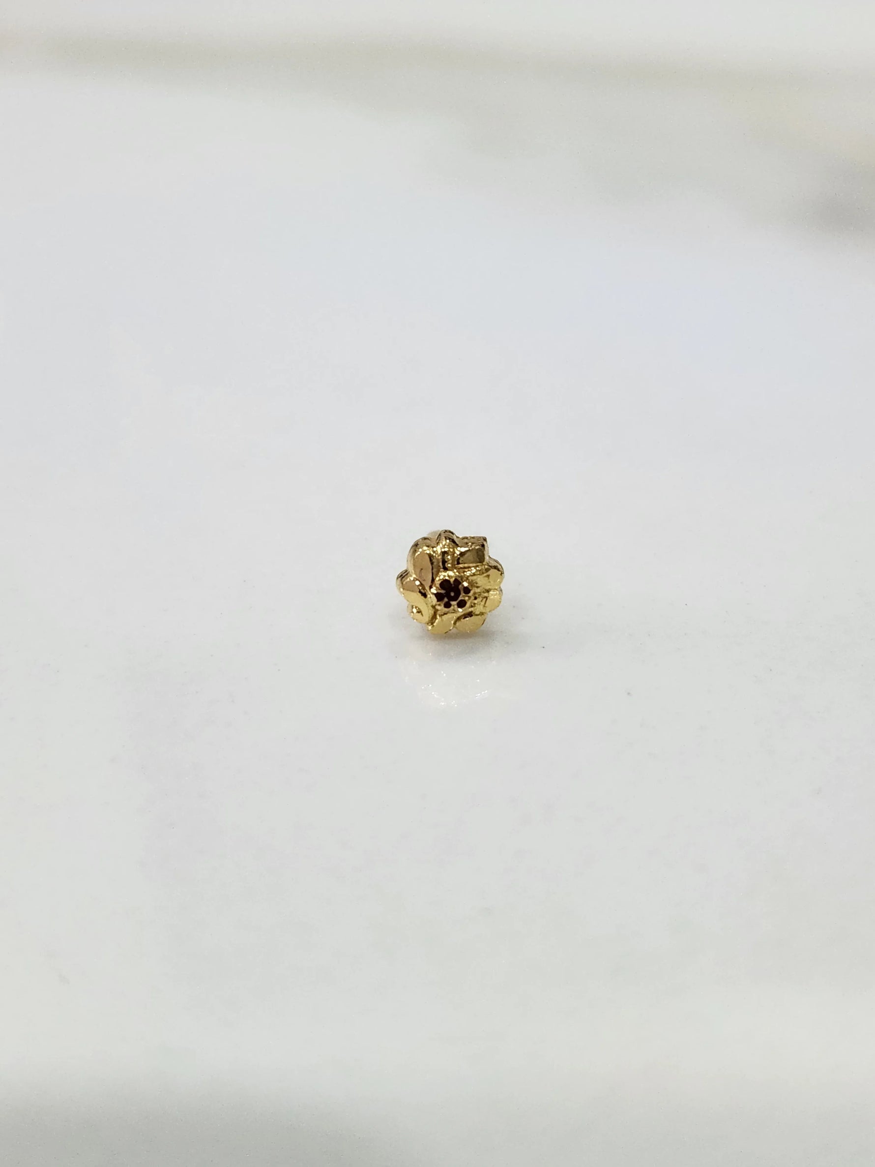 Side view of a delicate gold nose pin on a white surface highlighting fine detailing and shape