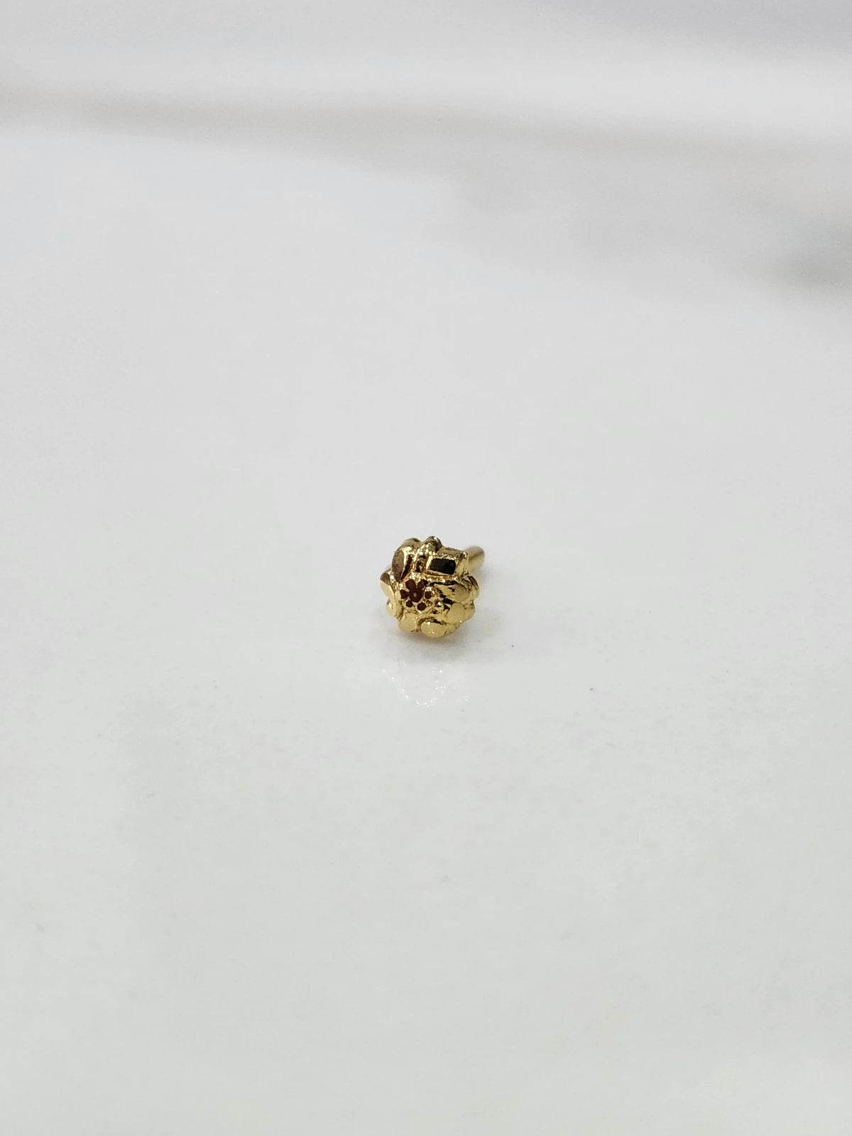 Front view of a tiny gold nose pin placed on a white background showing its compact size
