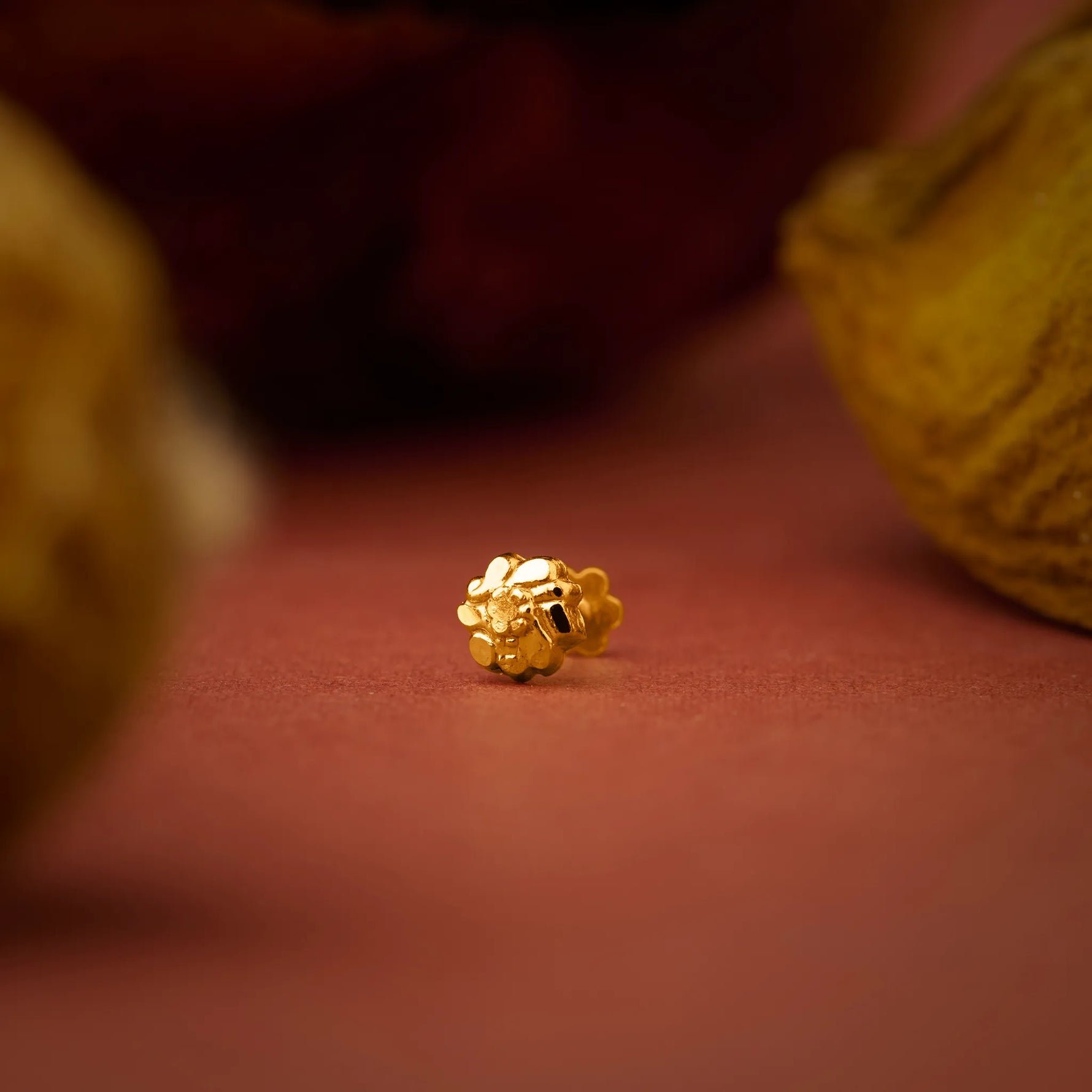 Close up of a small gold nose pin placed on a warm textured surface highlighting its polished finish
