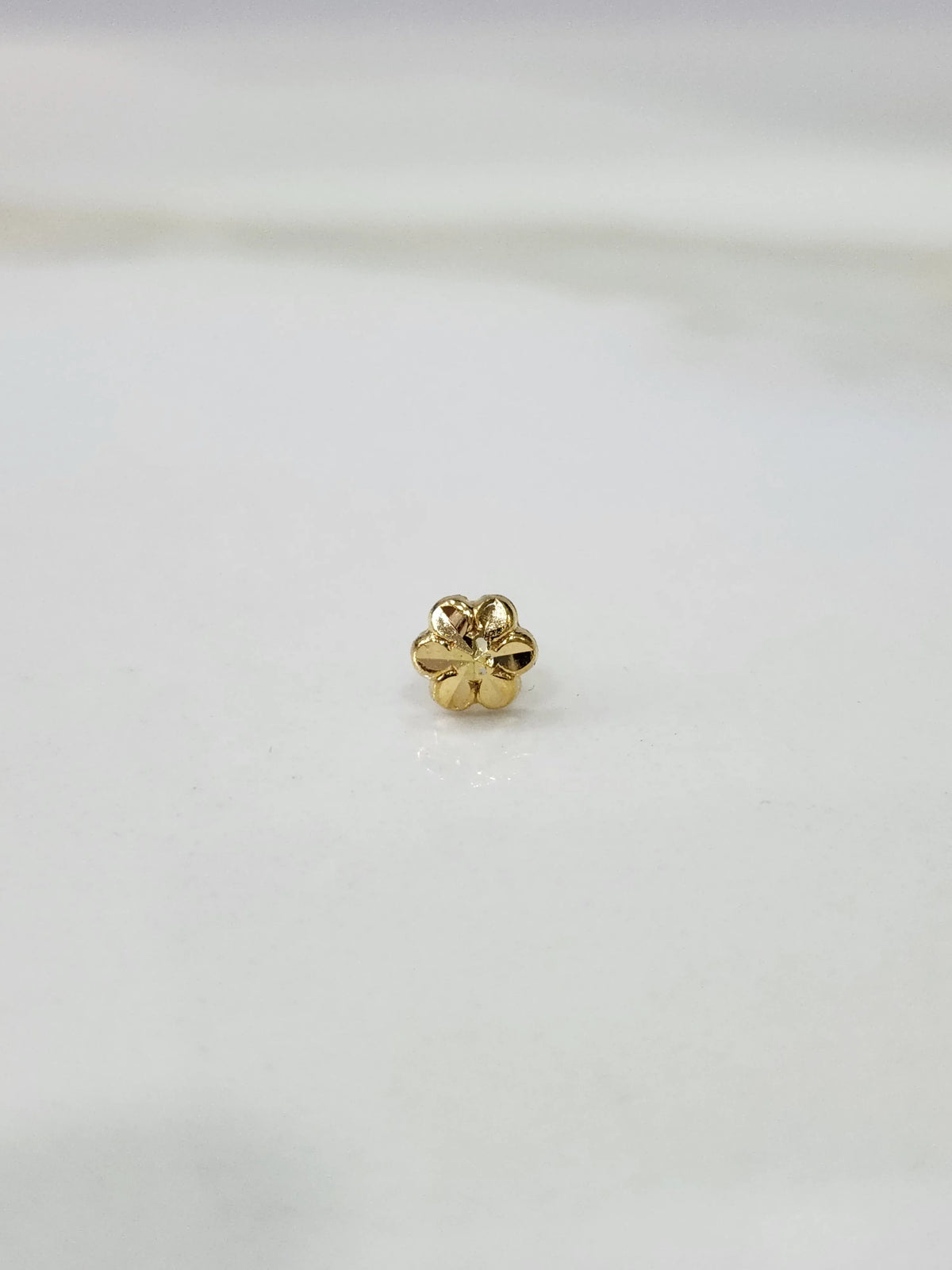 Small gold nose pin placed on a white background showing fine detailing and compact round shape