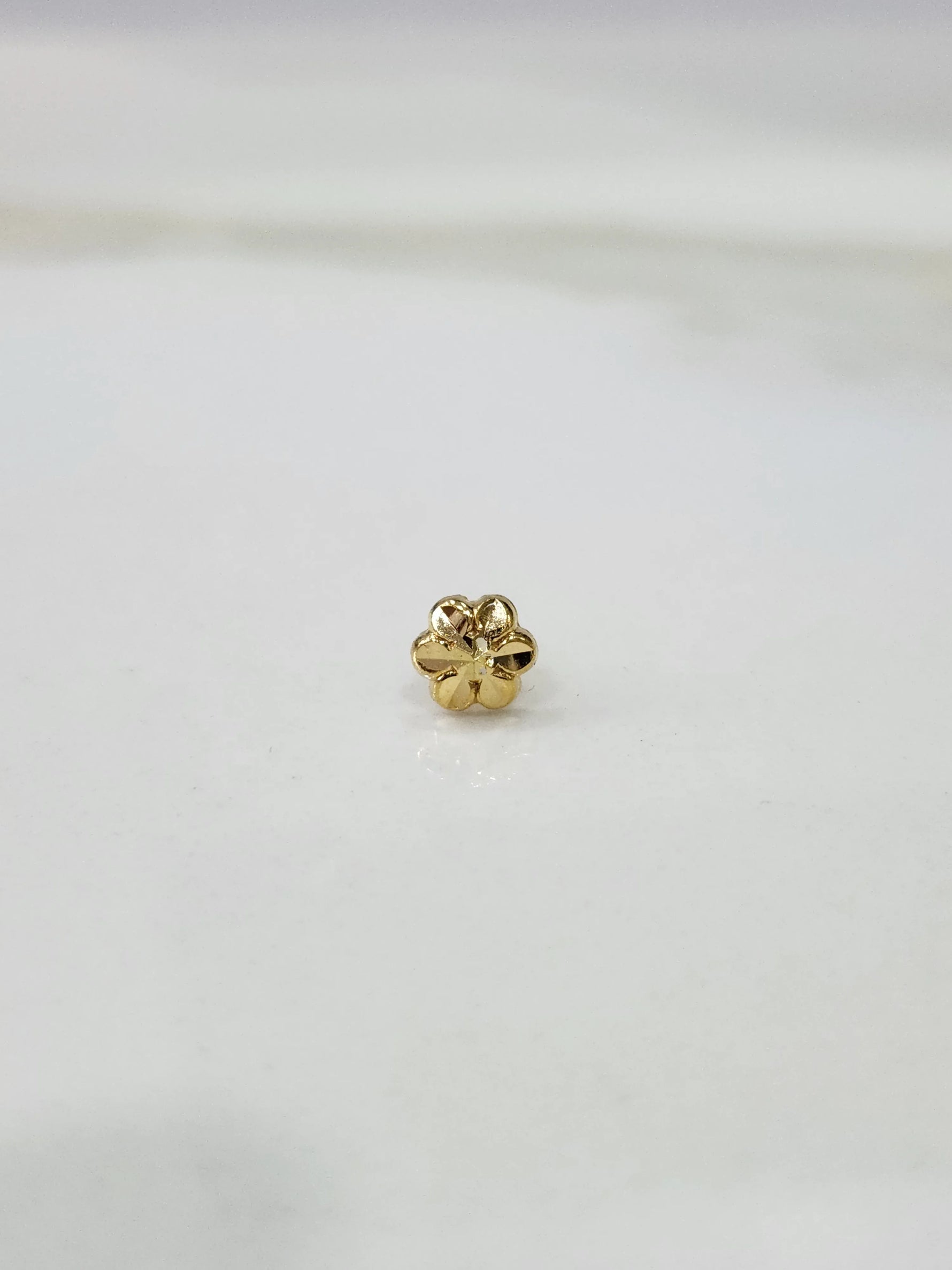 Small gold nose pin placed on a white background showing fine detailing and compact round shape