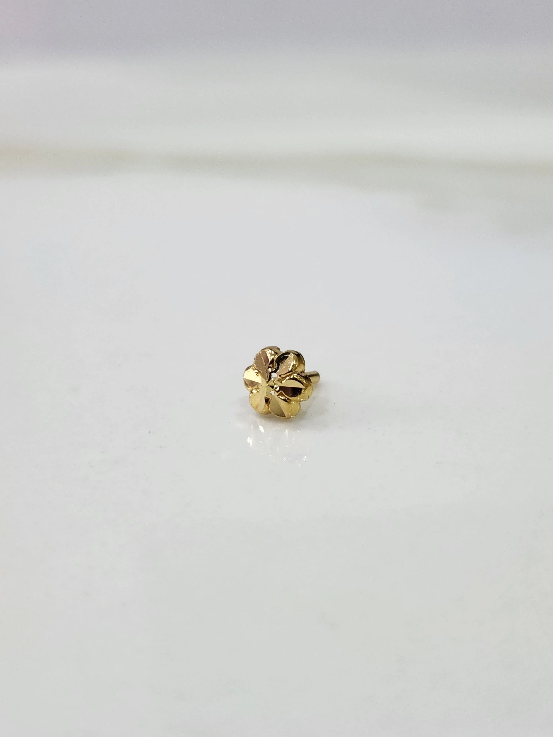 Side view of a tiny gold nose pin on a white surface highlighting its subtle shine and minimal form
