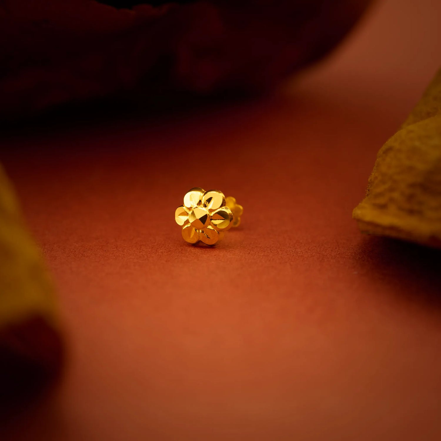Close up of a small floral gold nose pin placed on a warm brown surface highlighting its polished finish and intricate design