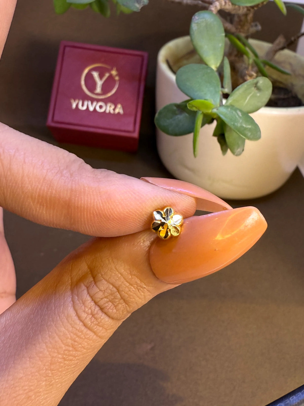Hand holding a tiny gold nose pin near a Yuvora box showing its lightweight size and wearable scale