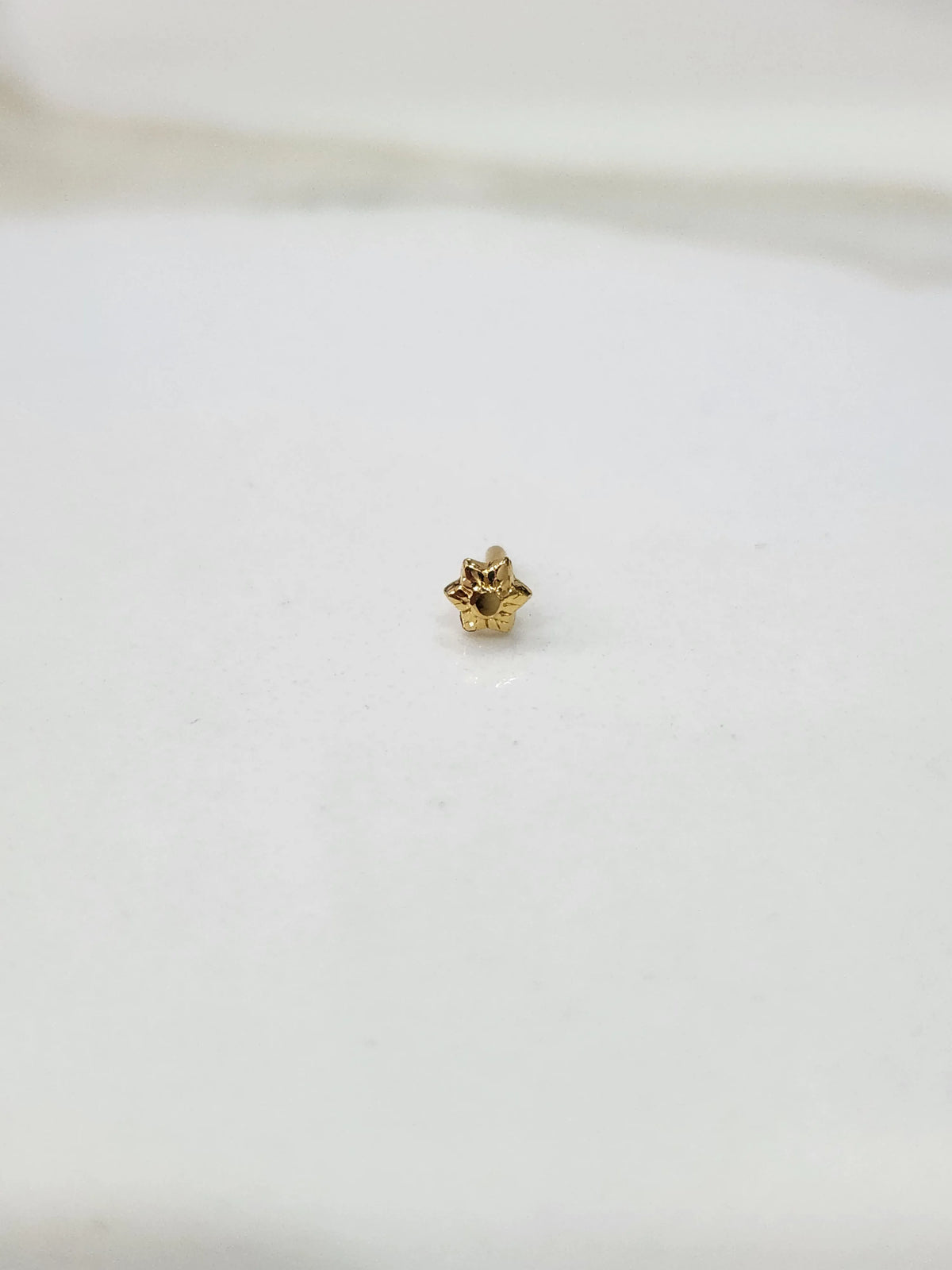 Side view of a small gold nose pin on a white surface highlighting its minimalist design and smooth shine