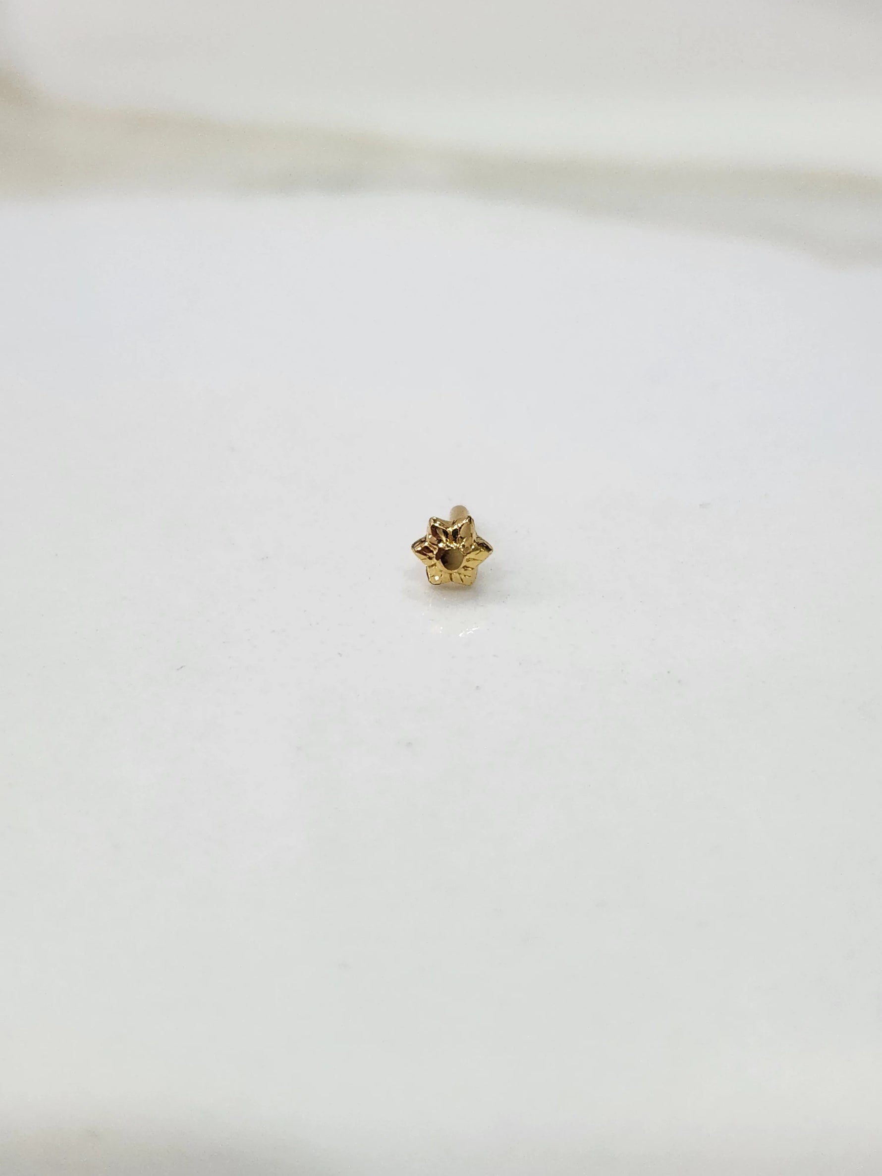Side view of a small gold nose pin on a white surface highlighting its minimalist design and smooth shine