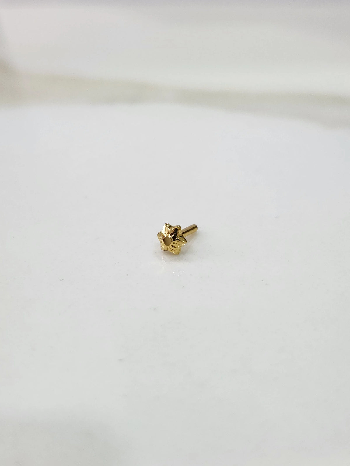 Tiny gold nose pin placed on a white background showing its compact size and fine detailing