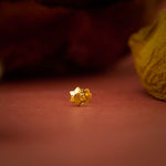 Close up of a small gold nose pin placed on a warm brown surface highlighting its intricate shape and polished finish