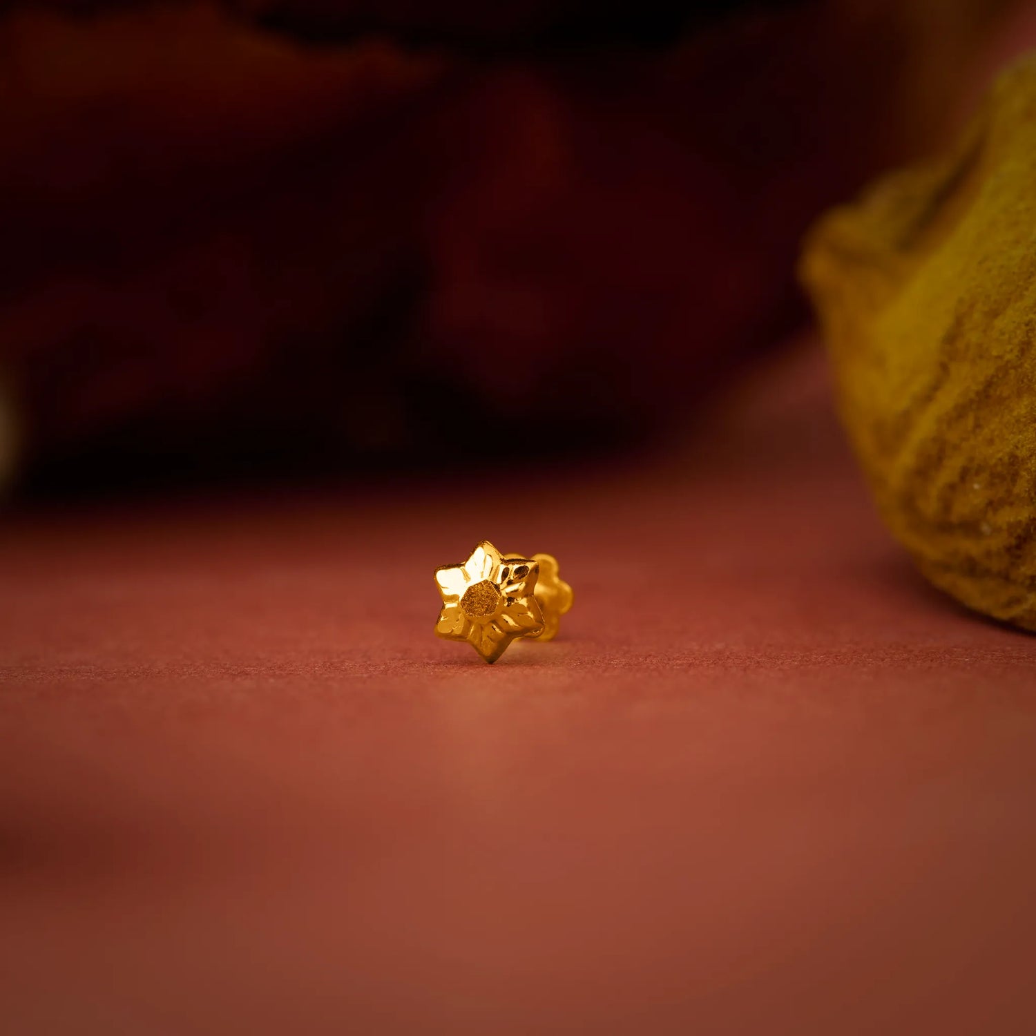 Close up of a small gold nose pin placed on a warm brown surface highlighting its intricate shape and polished finish