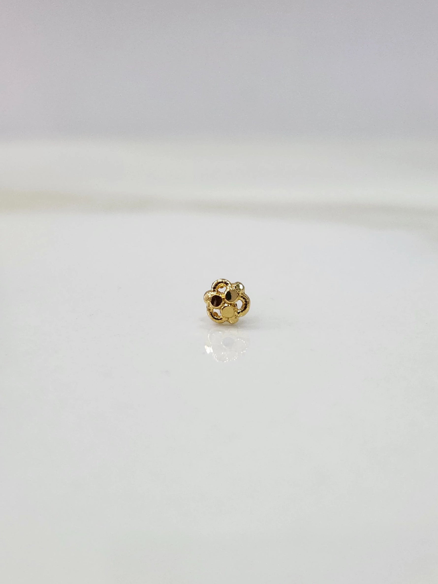 Side view of the floral 18K gold nose pin on a white surface showing depth and craftsmanship