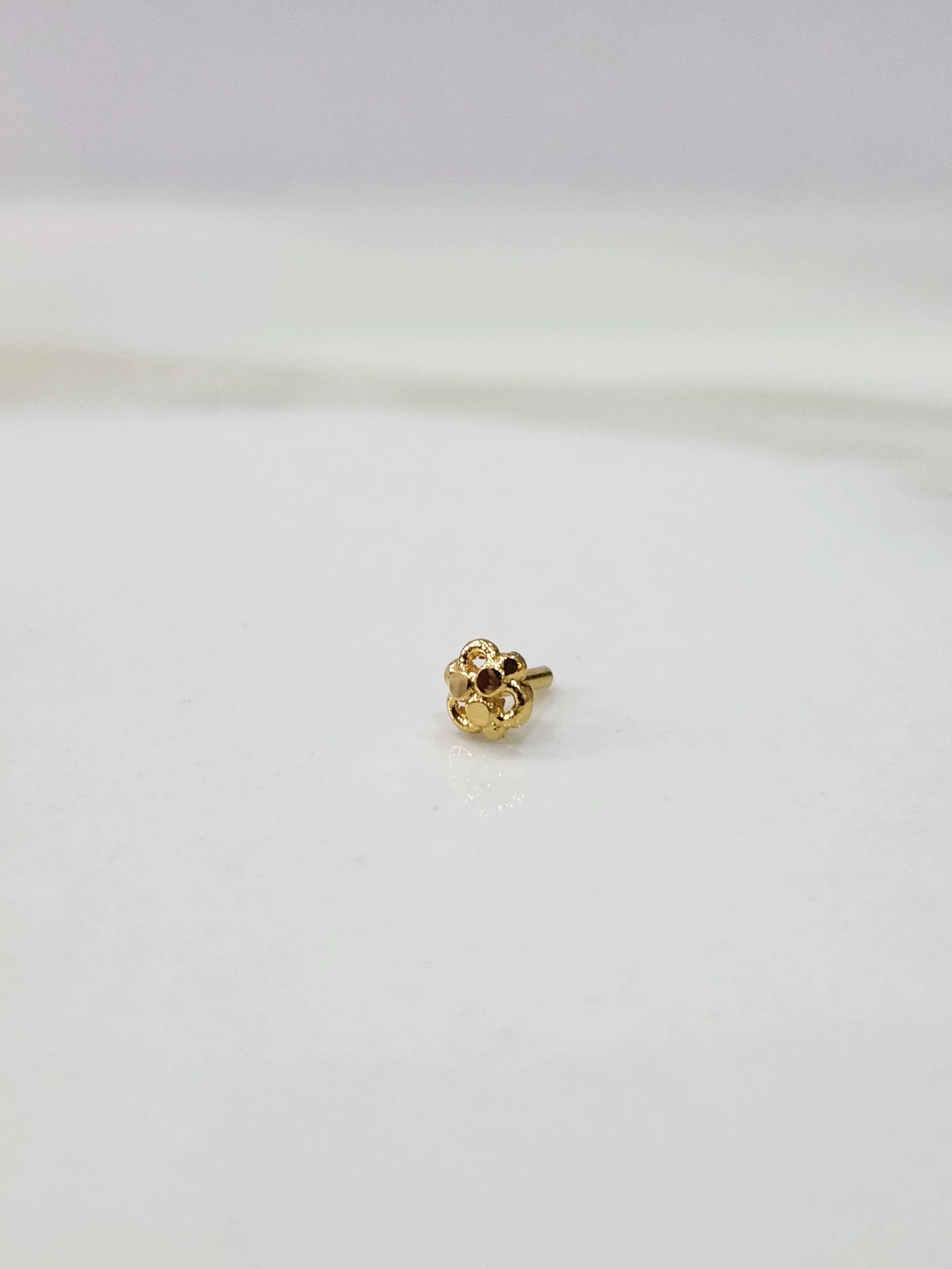 Front view of a floral 18K gold nose pin placed on a white background highlighting its design
