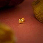 Close up view of a floral 18K gold nose pin placed on a warm red surface highlighting fine detailing