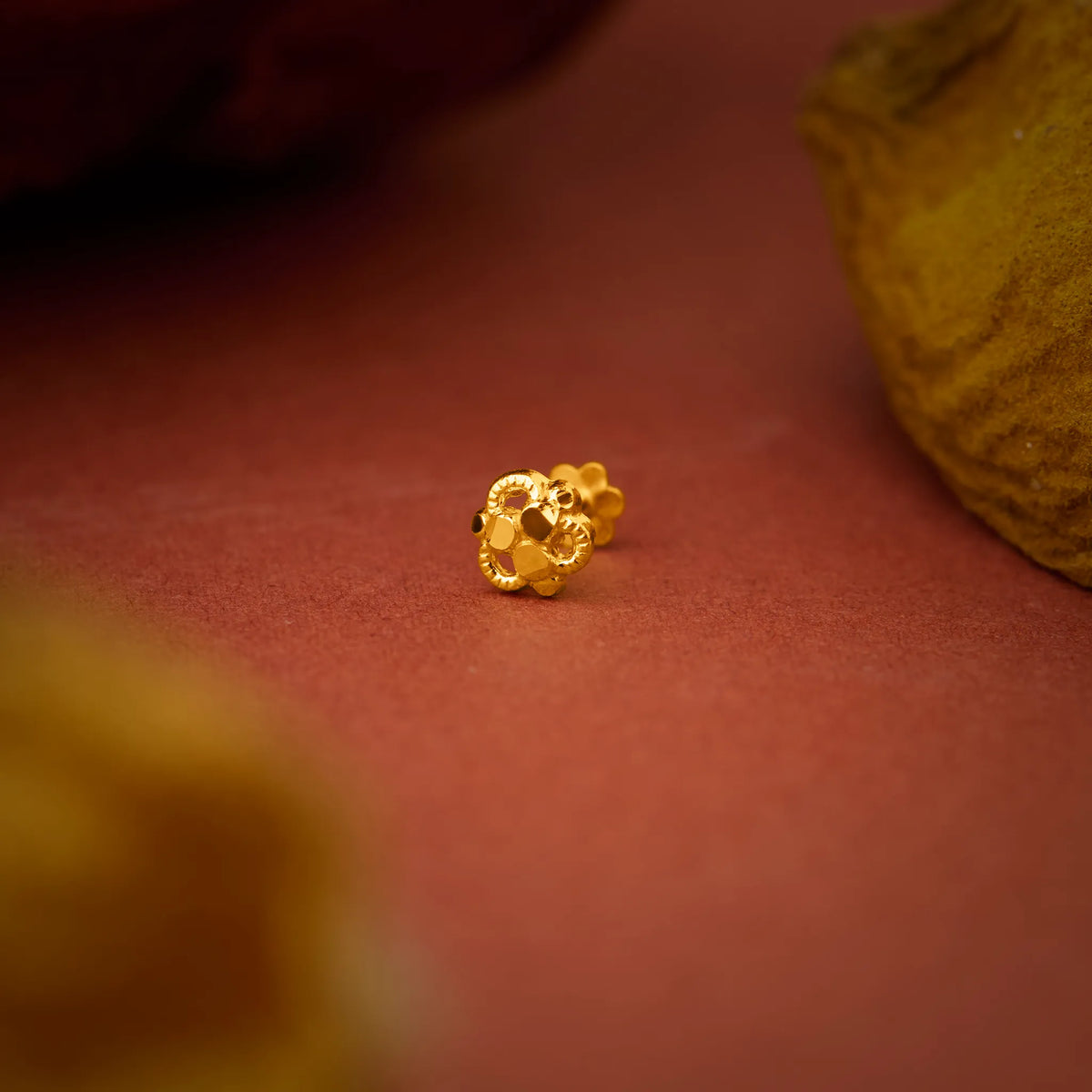 Close up view of a floral 18K gold nose pin placed on a warm red surface highlighting fine detailing