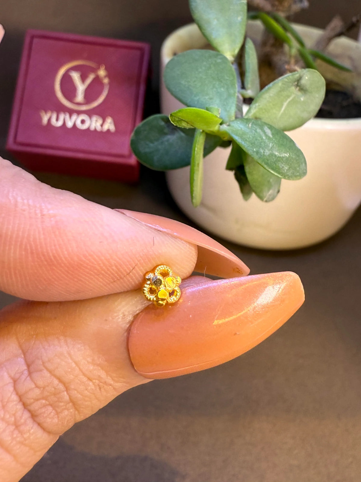 Hand holding a floral gold nose pin near a plant to show real size and wearability