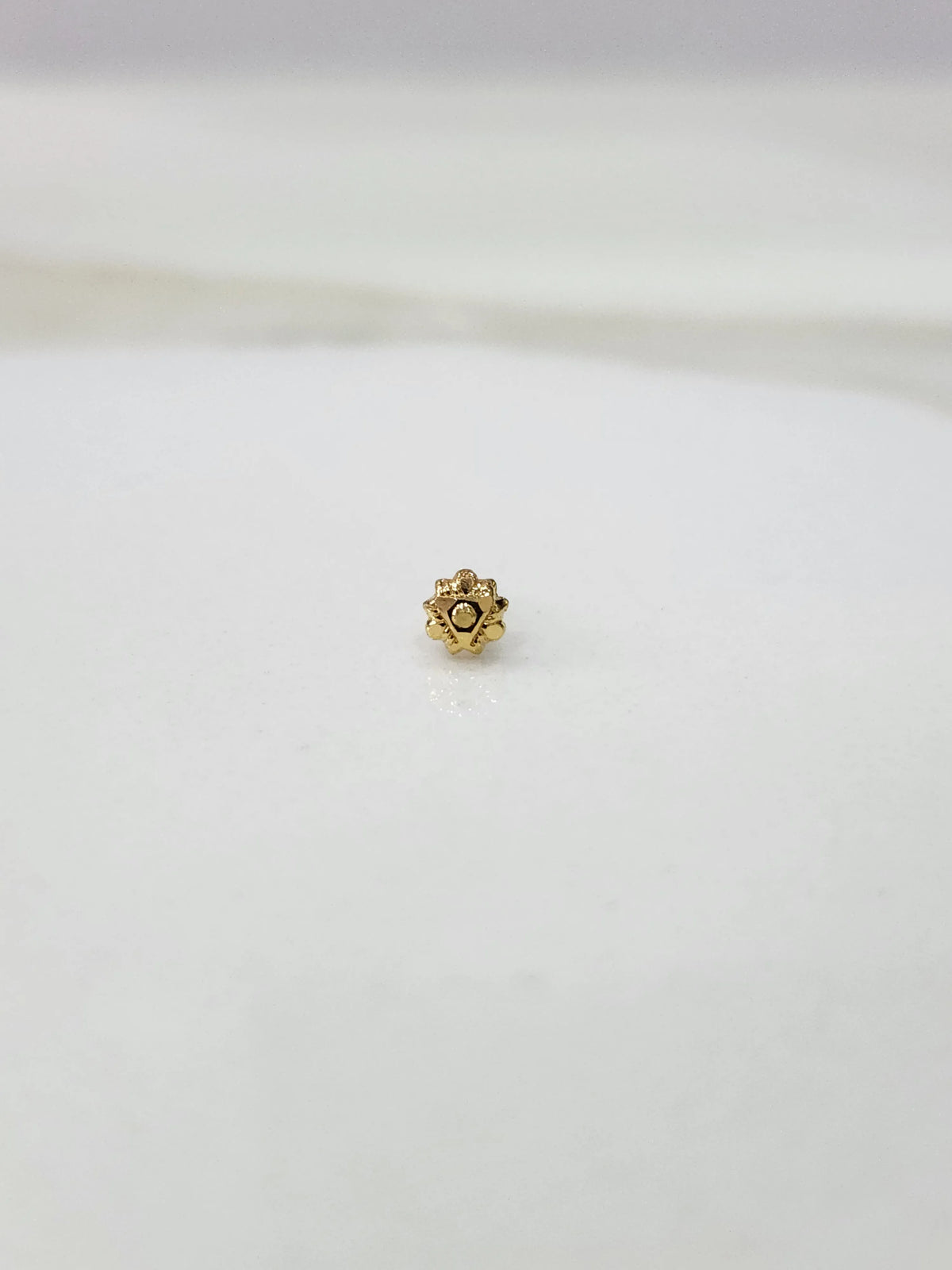 Side view of a minimal gold nose pin on a white surface highlighting its subtle shine and neat finish