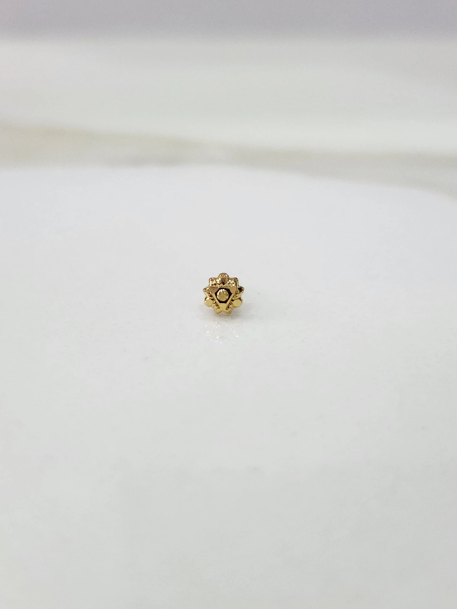 Side view of a minimal gold nose pin on a white surface highlighting its subtle shine and neat finish