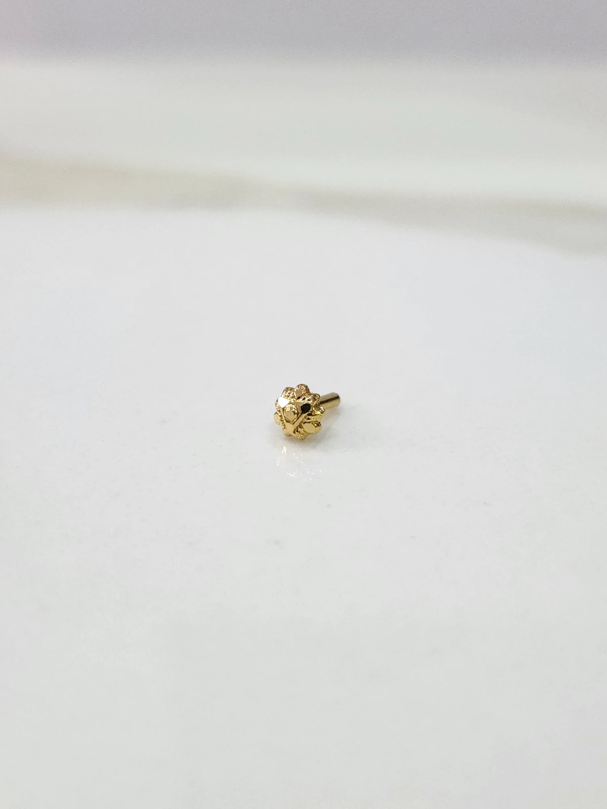 Small gold nose pin placed on a white background displaying fine detailing and compact proportions