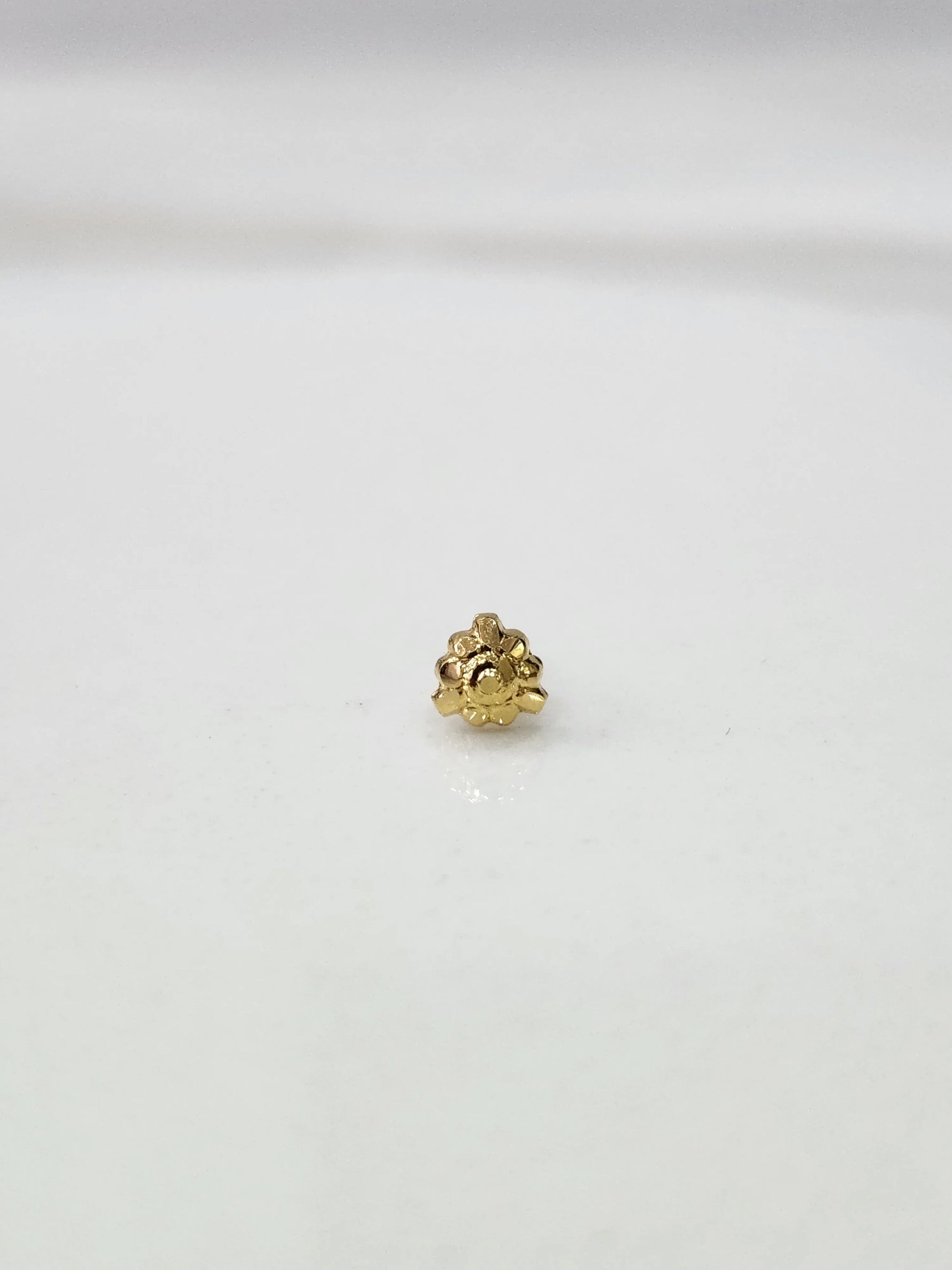 Side view of a lightweight gold nose pin on a white surface highlighting its fine craftsmanship and minimal profile