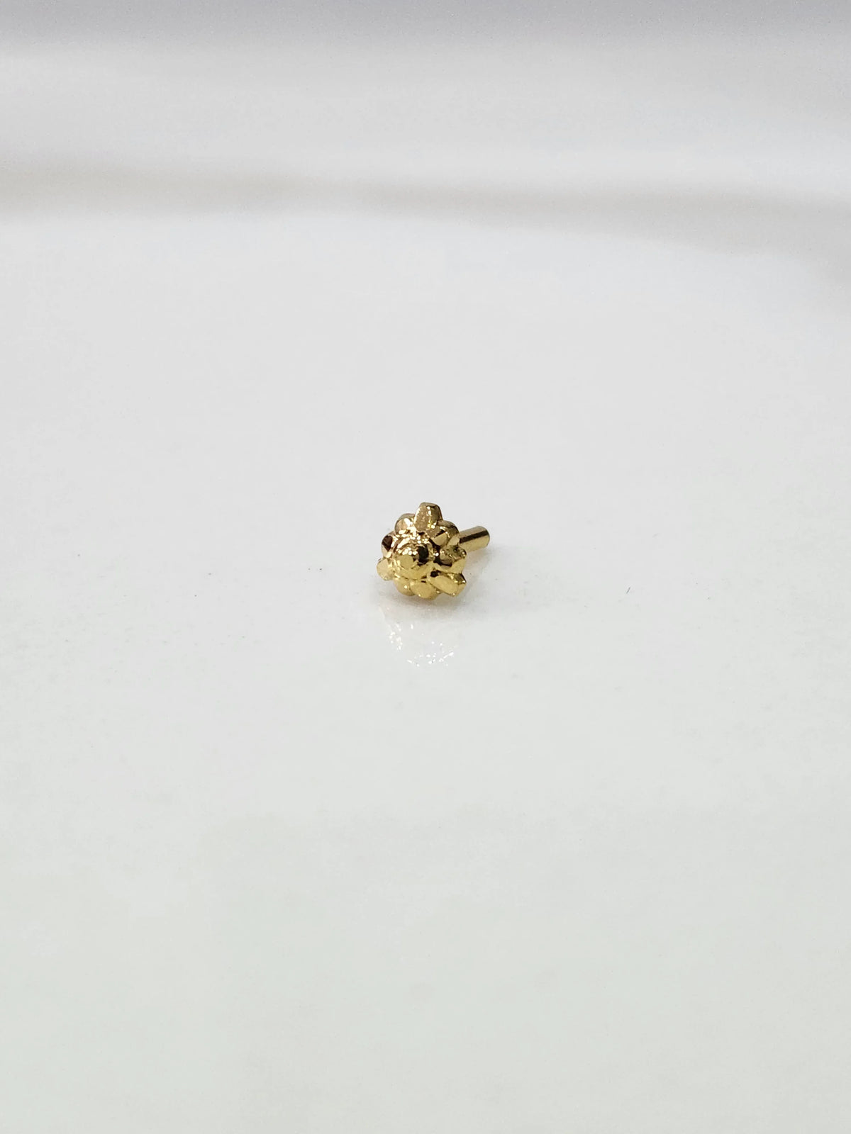 Front view of a tiny gold nose pin placed on a white background showing its compact size and neat design