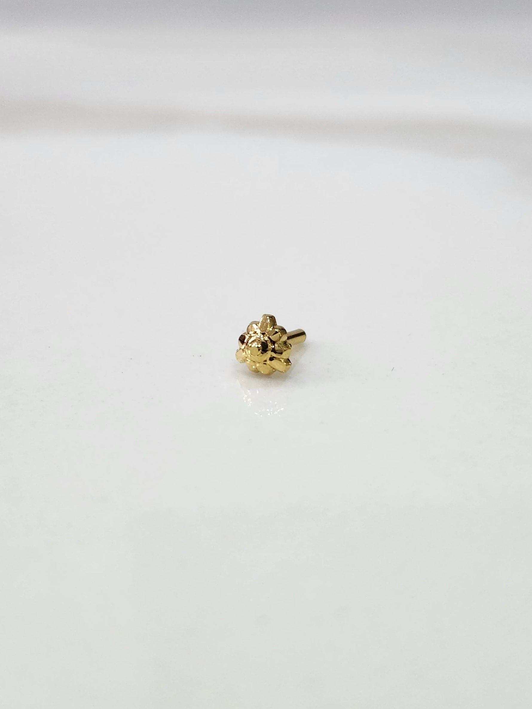 Front view of a tiny gold nose pin placed on a white background showing its compact size and neat design