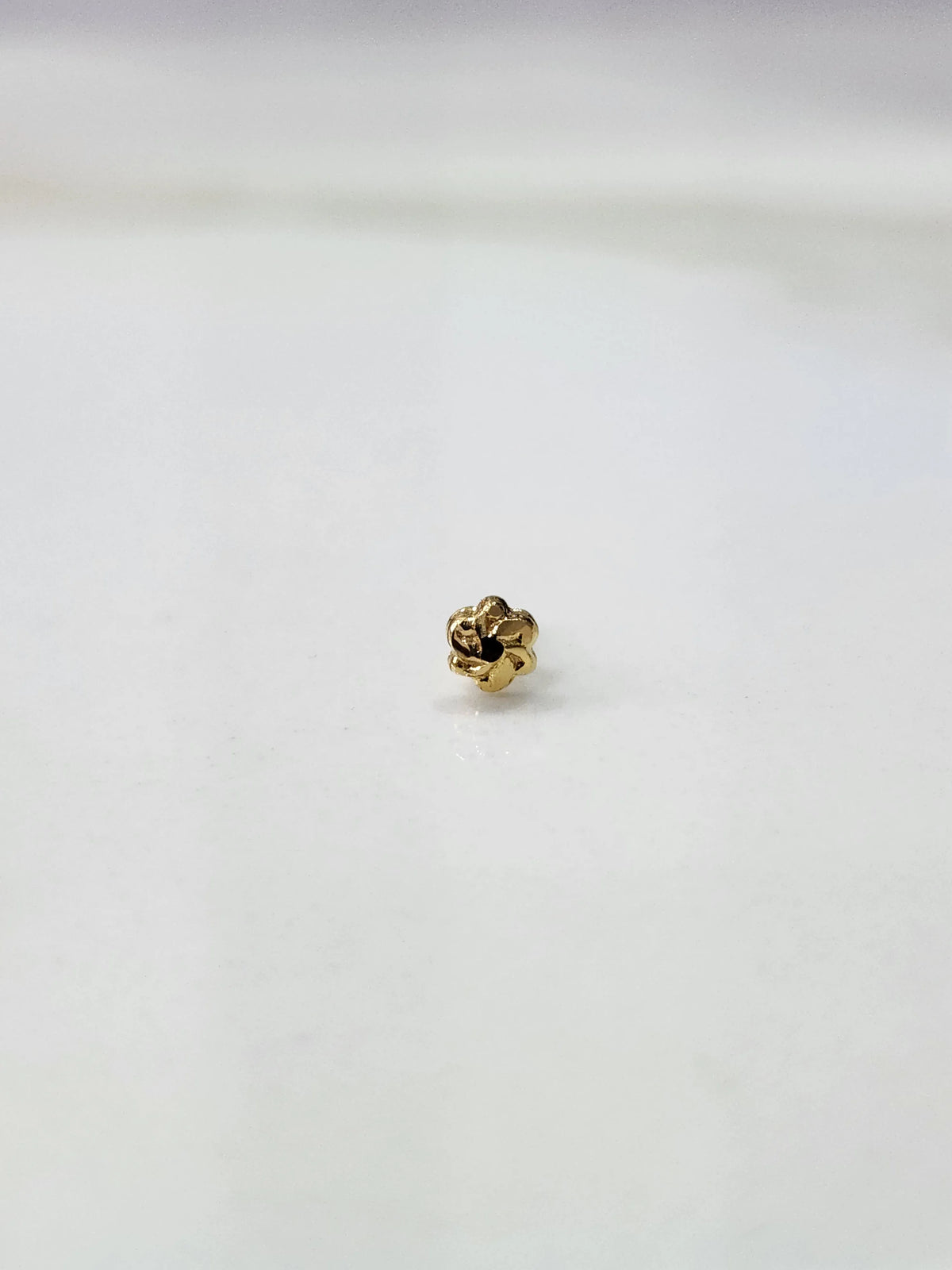 Slight side angled view of a small 18K gold nose pin placed on a white surface highlighting its subtle shine and craftsmanship