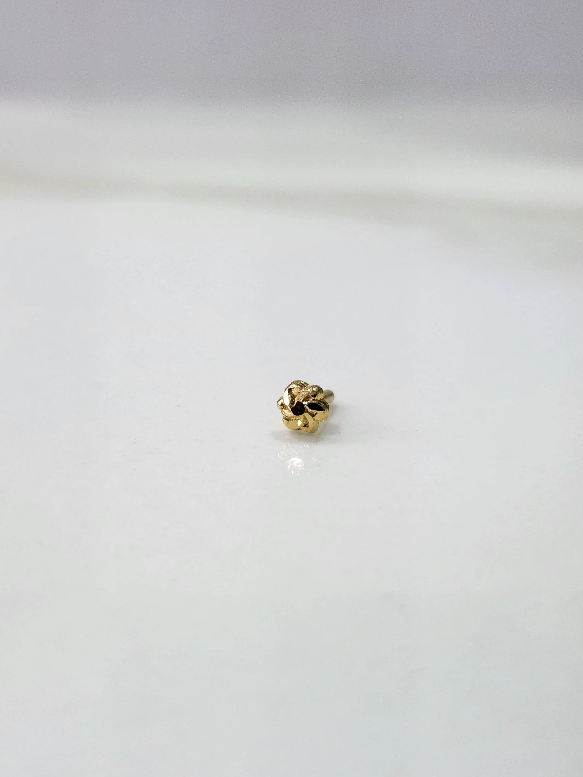 Front view of a tiny 18K gold nose pin on a white background showing its compact size and fine detailing