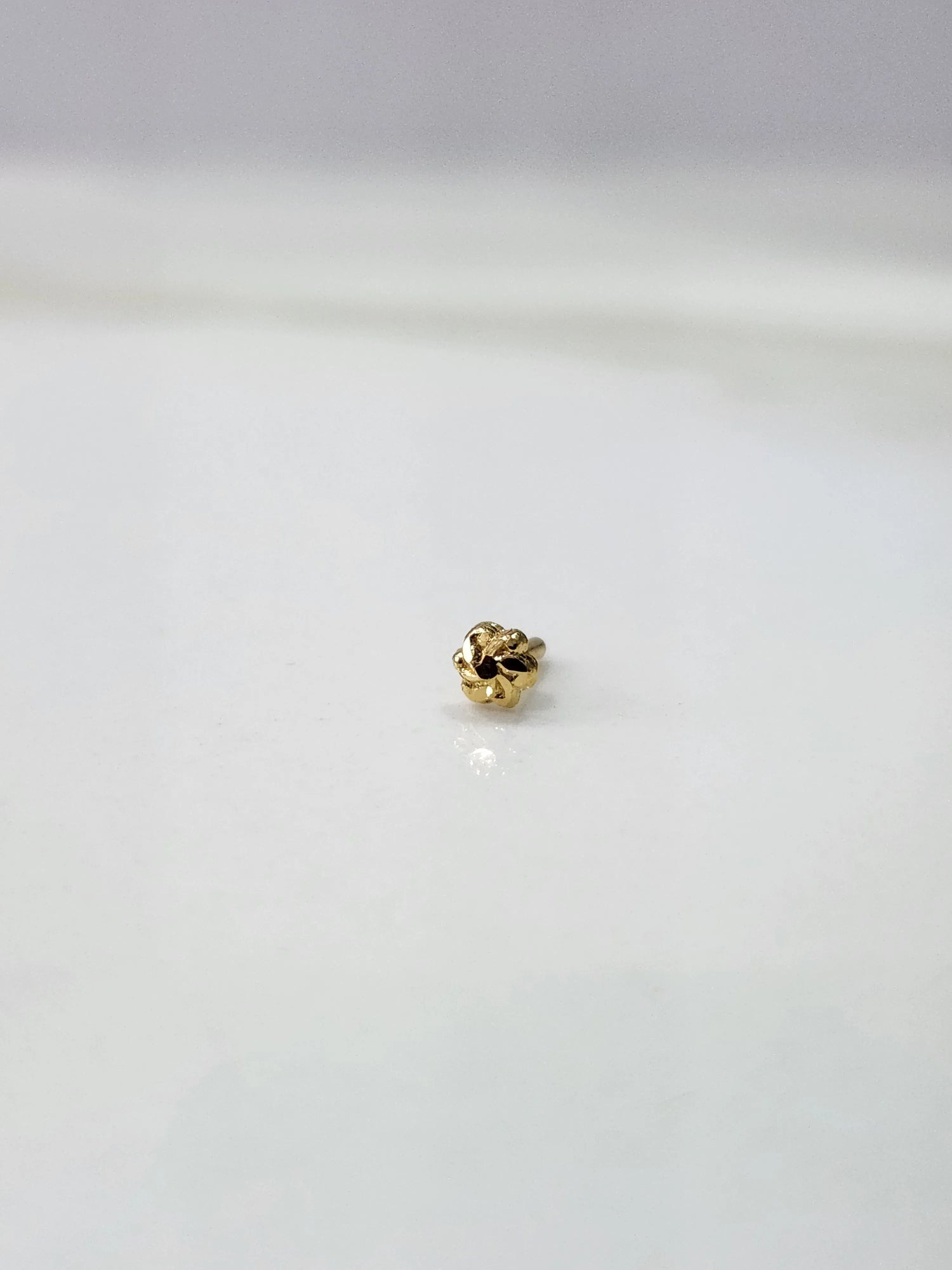 Front view of a tiny 18K gold nose pin on a white background showing its compact size and fine detailing