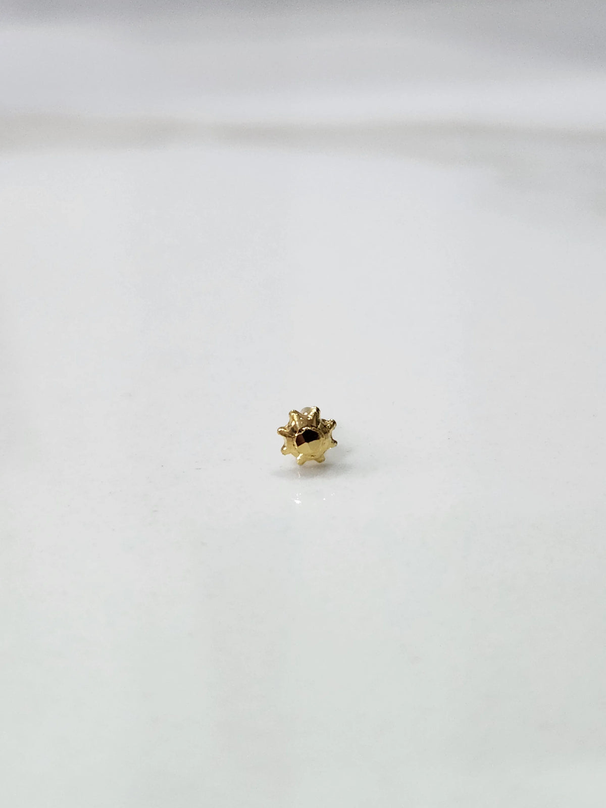 Side view of a lightweight gold nose pin on a white surface showing its compact size and fine finish