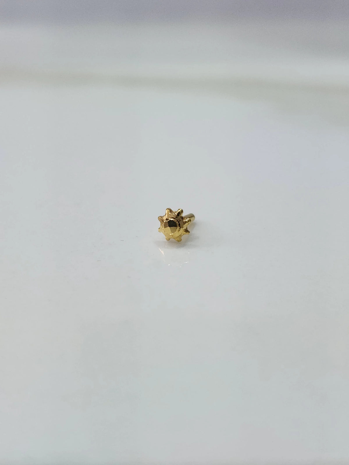 Front view of a tiny gold nose pin placed on a white background highlighting its minimal design