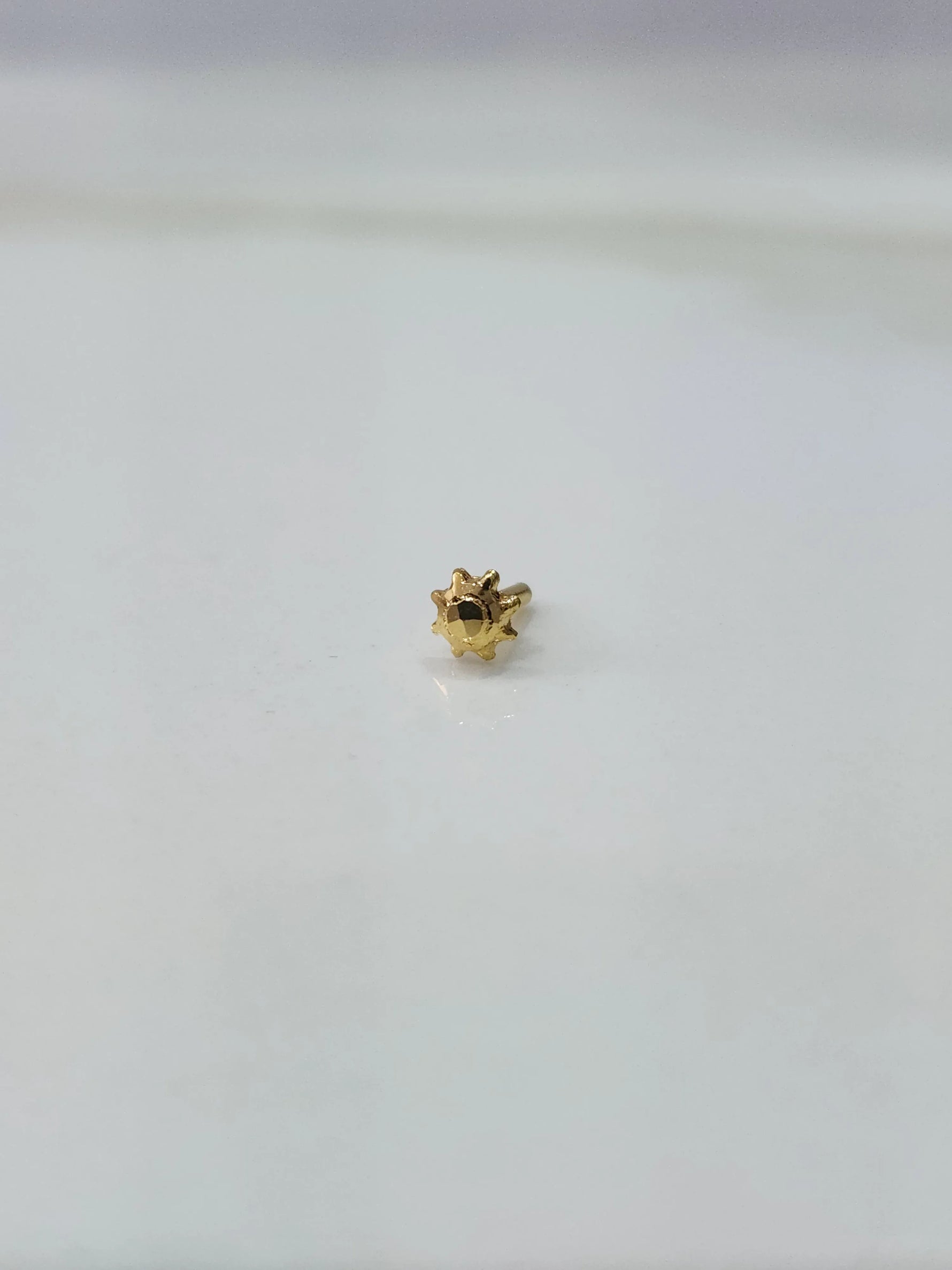 Front view of a tiny gold nose pin placed on a white background highlighting its minimal design