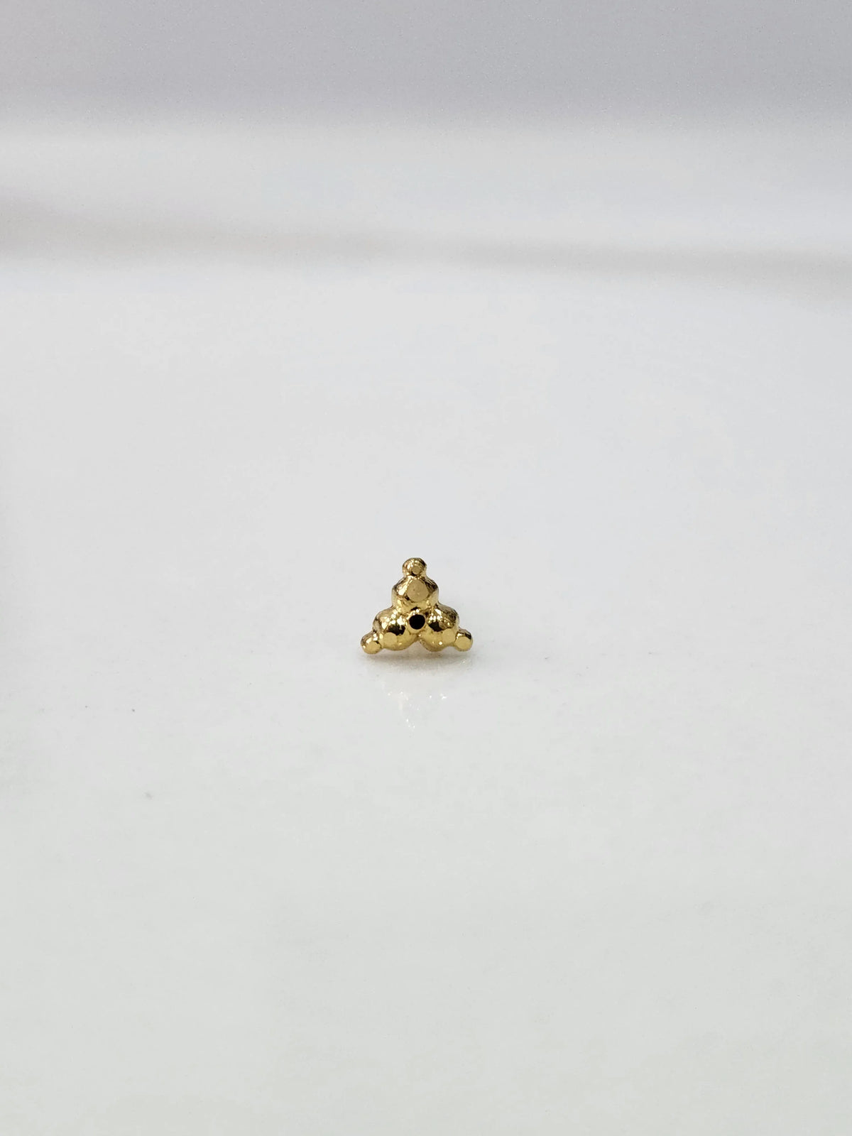 Side angle view of small 18k gold nose pin on white surface for clearer detailing