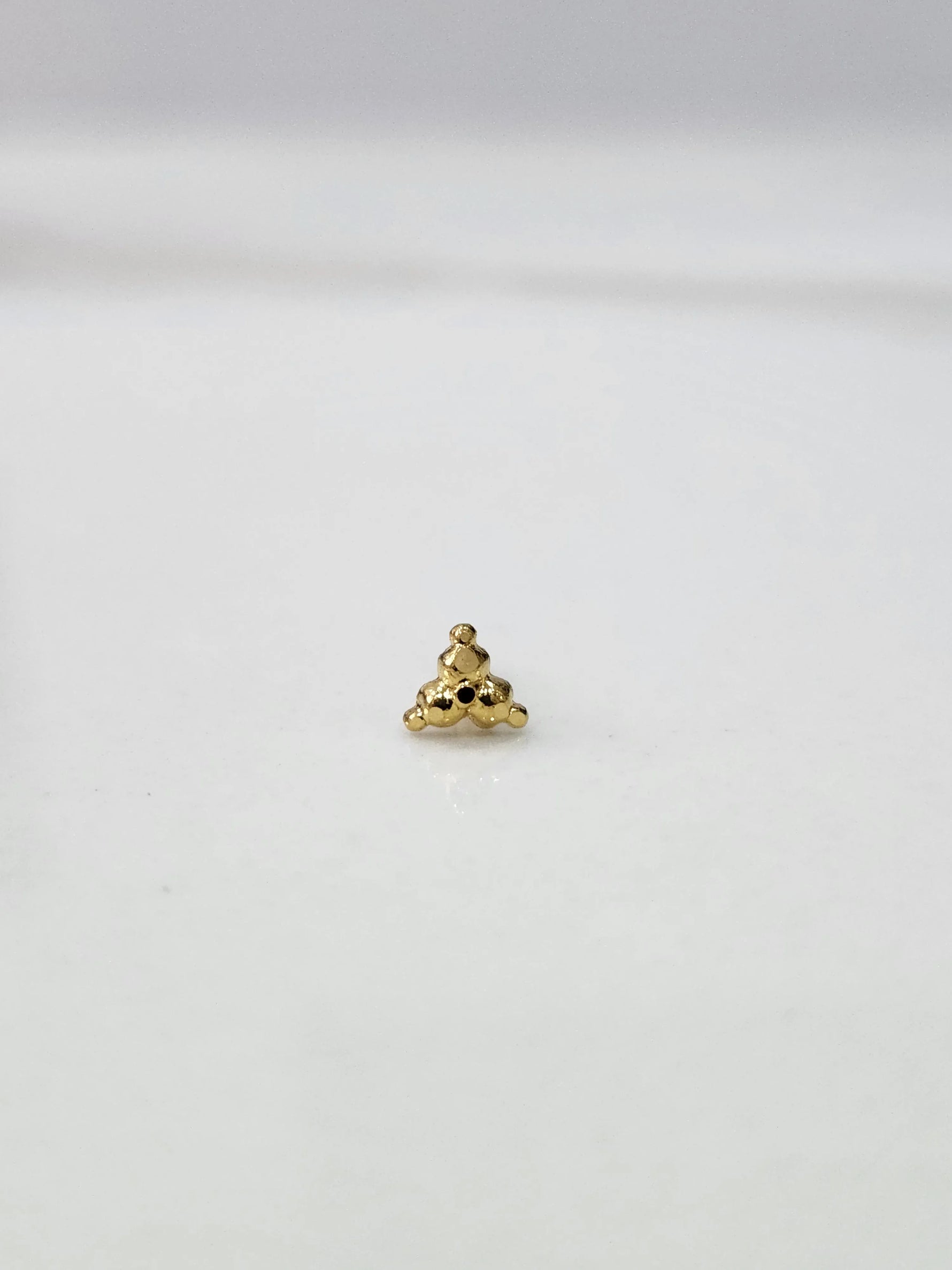 Side angle view of small 18k gold nose pin on white surface for clearer detailing