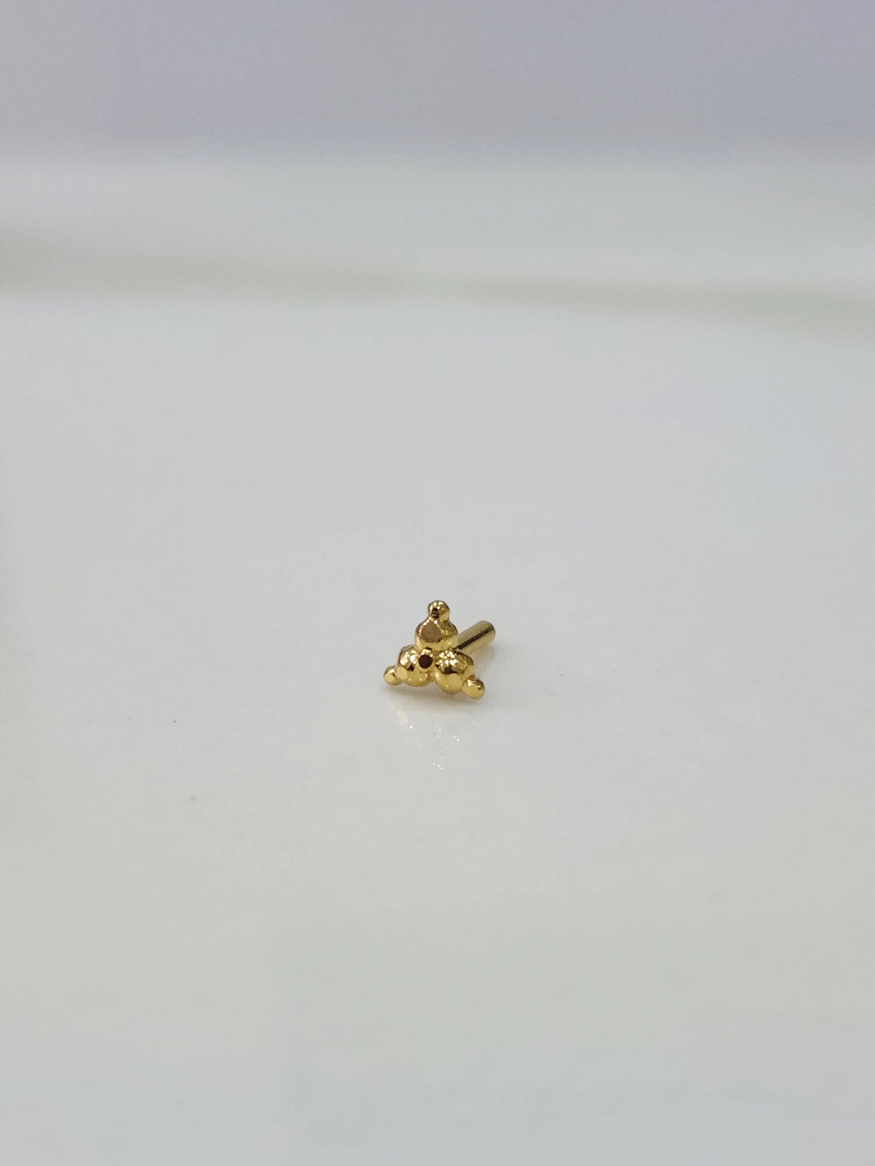 Close-up of tiny gold nose pin placed on white surface showing detailed design