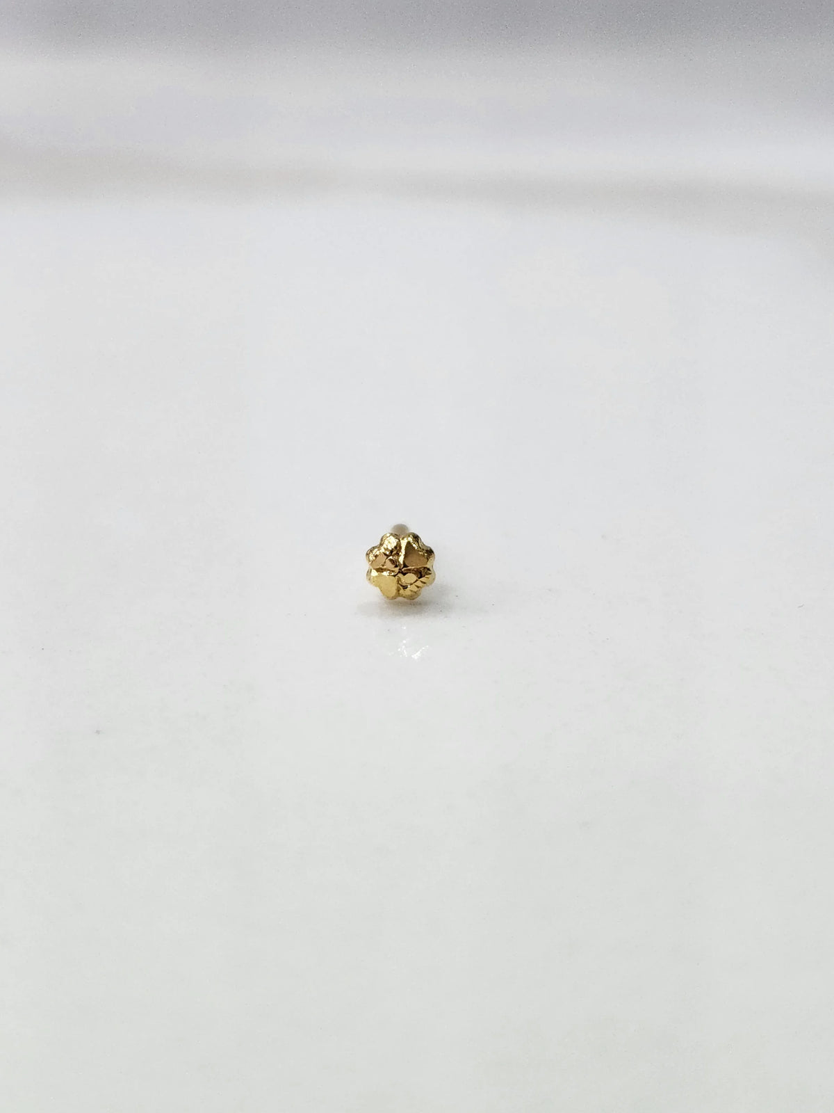 Side view of a lightweight gold nose pin on a white surface emphasizing its compact size and smooth finish