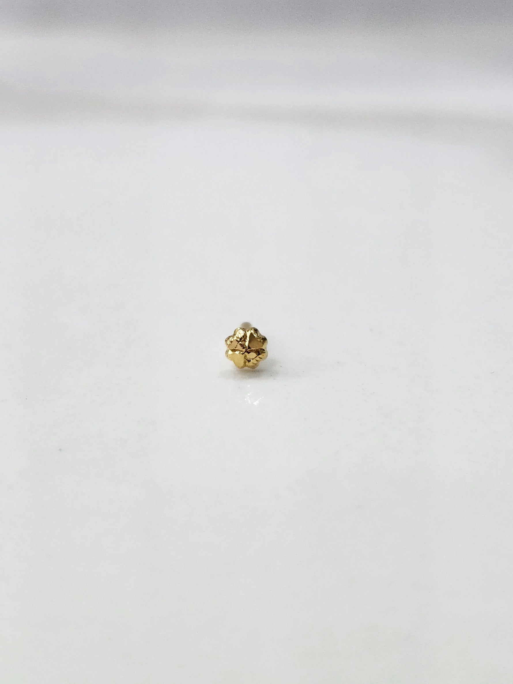 Side view of a lightweight gold nose pin on a white surface emphasizing its compact size and smooth finish