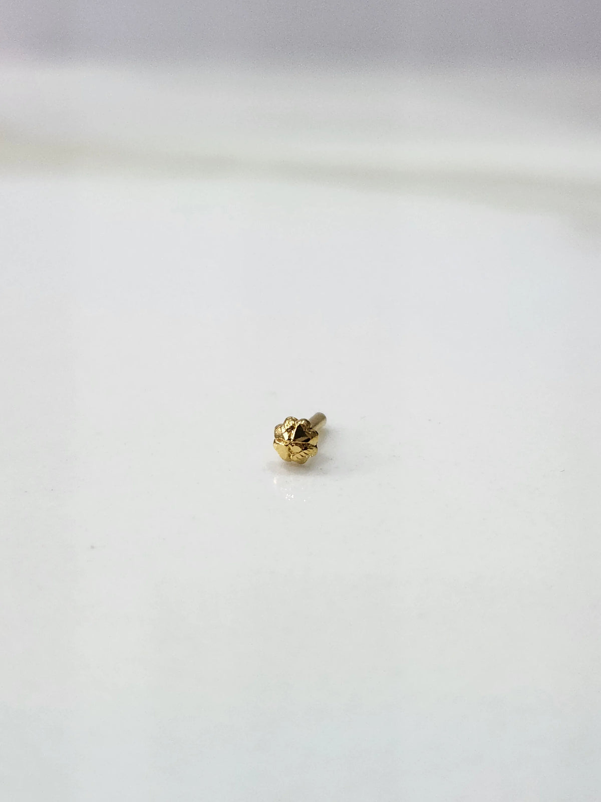 Front view of a delicate gold nose pin placed on a white background showing fine craftsmanship