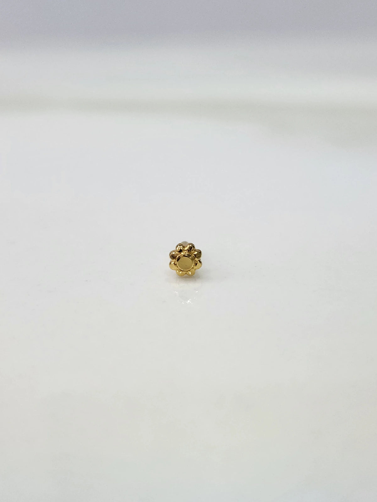 Side view of a tiny gold nose pin on a white surface emphasizing fine craftsmanship