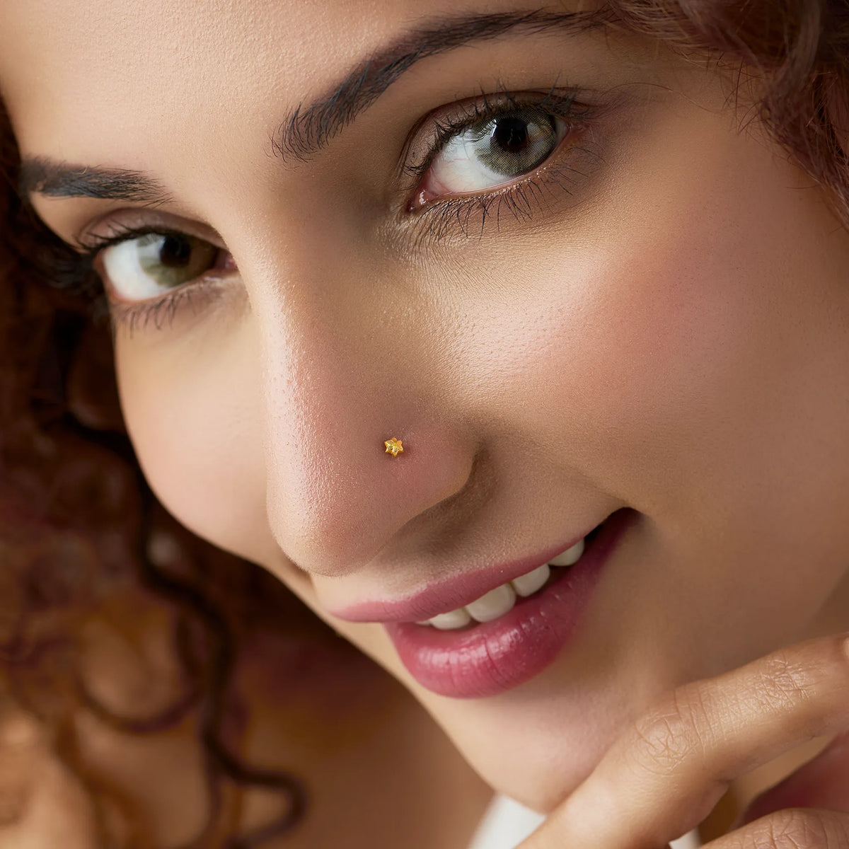 Woman wearing a small 18K gold nose pin shown in a soft front angle highlighting an elegant everyday look