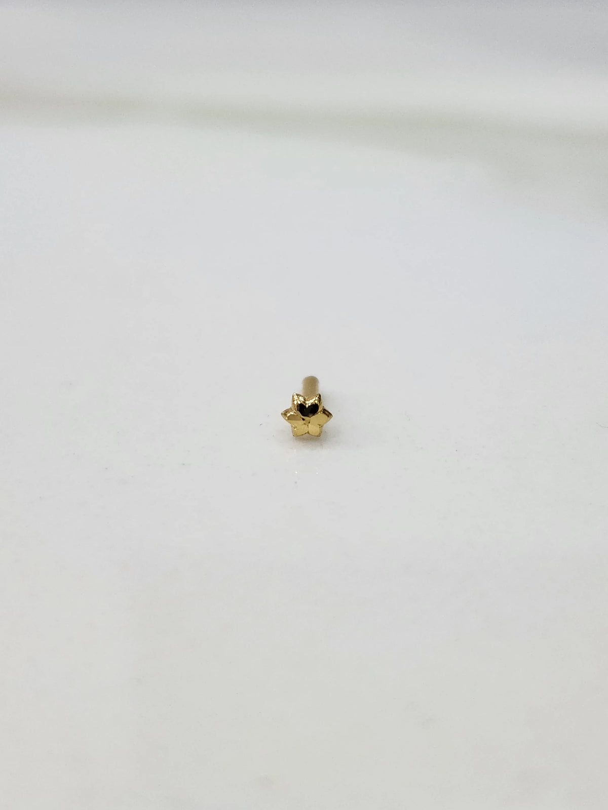 Slight angled view of a small 18K gold nose pin on a white surface highlighting its lightweight structure and polished finish