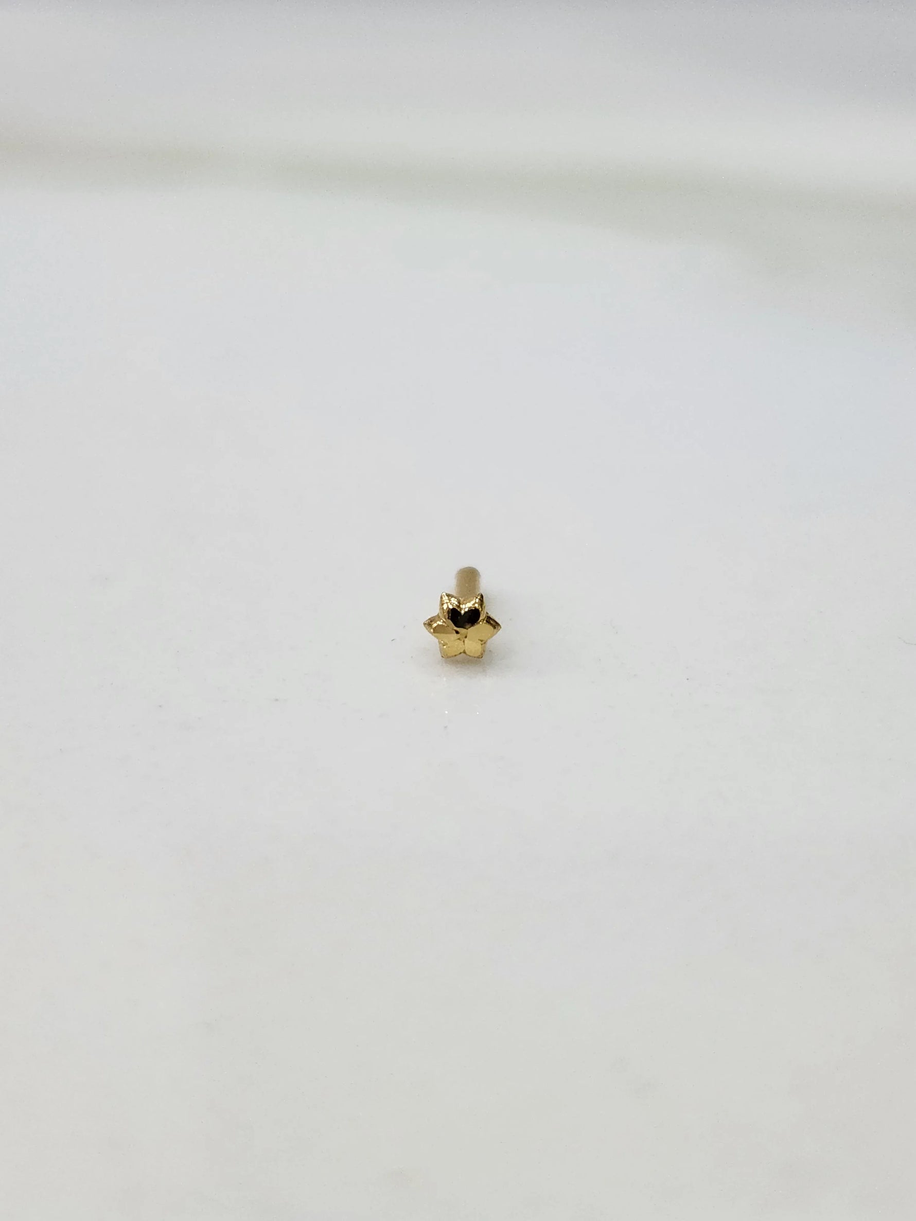 Slight angled view of a small 18K gold nose pin on a white surface highlighting its lightweight structure and polished finish