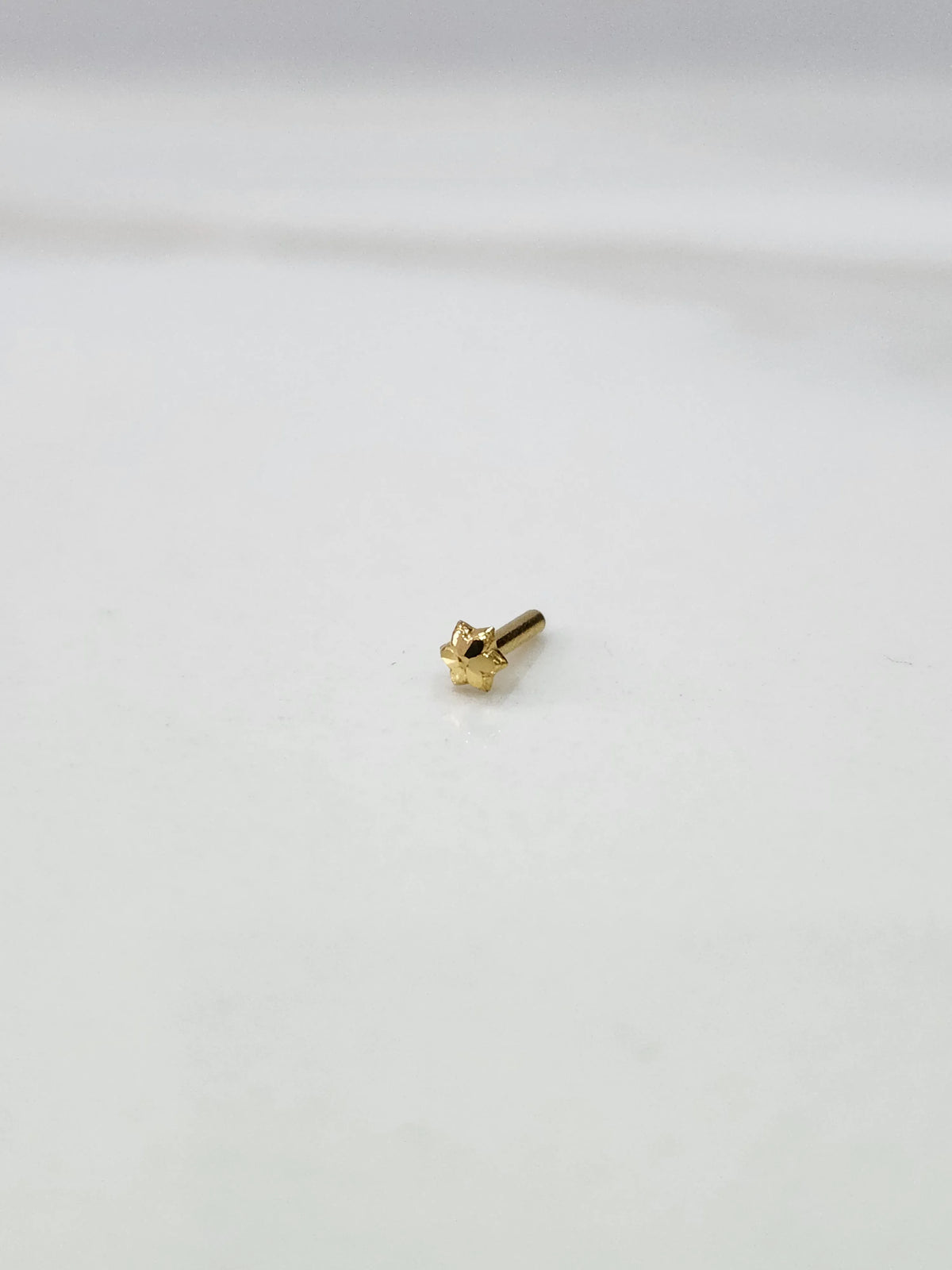 Front view of a tiny 18K gold nose pin placed on a white background showing its compact size and fine detailing