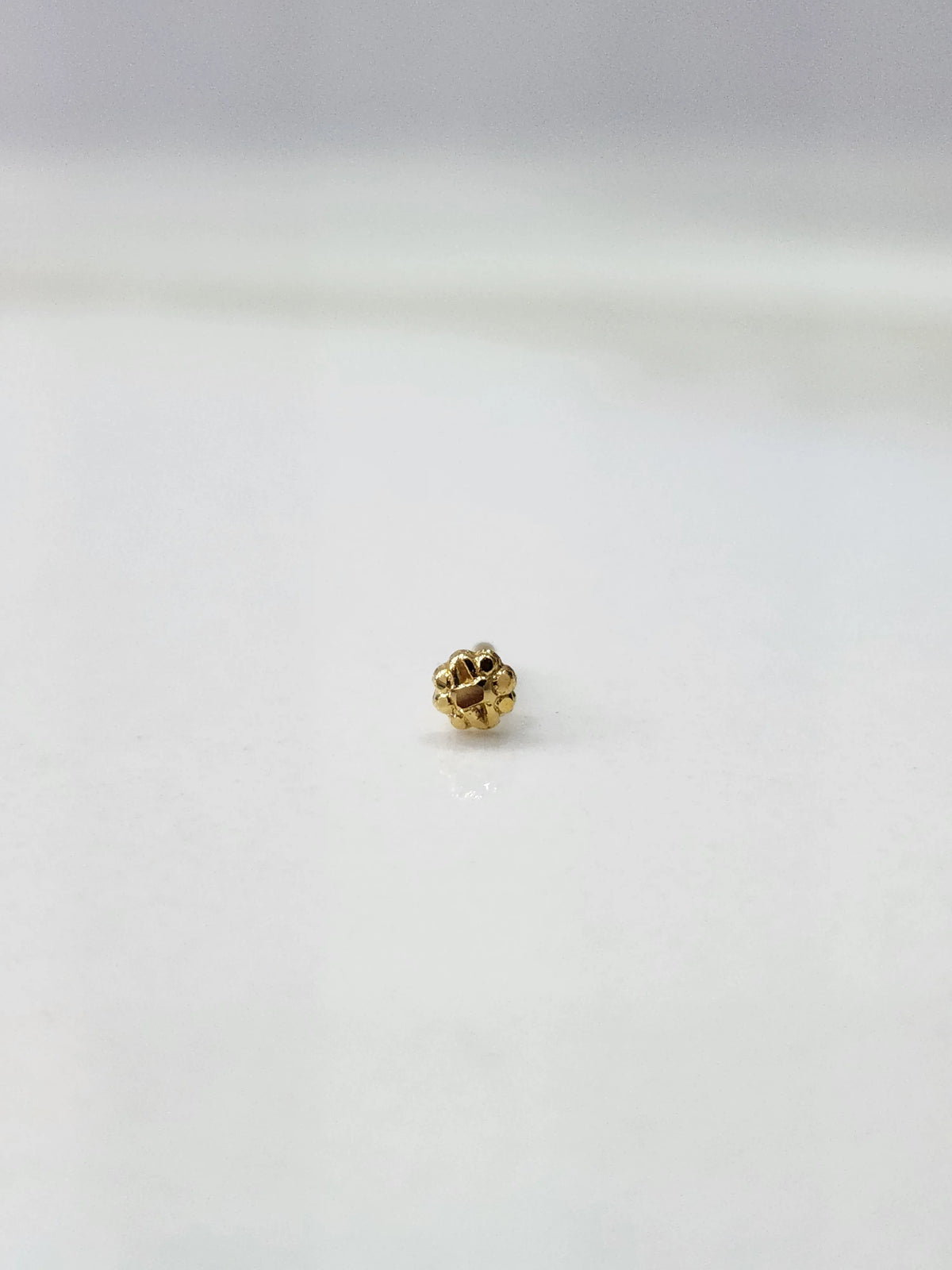 Side view of a delicate gold nose pin on a white surface showing its lightweight structure and fine detailing