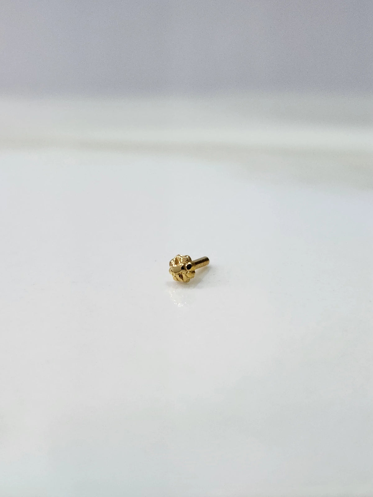 Front view of a tiny gold nose pin placed on a white background highlighting its minimal design and size