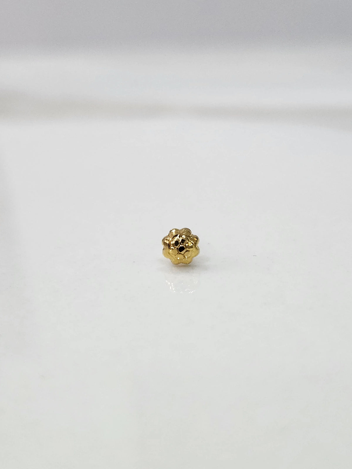 Side view of a gold nose pin on a white surface showing its compact size and polished finish