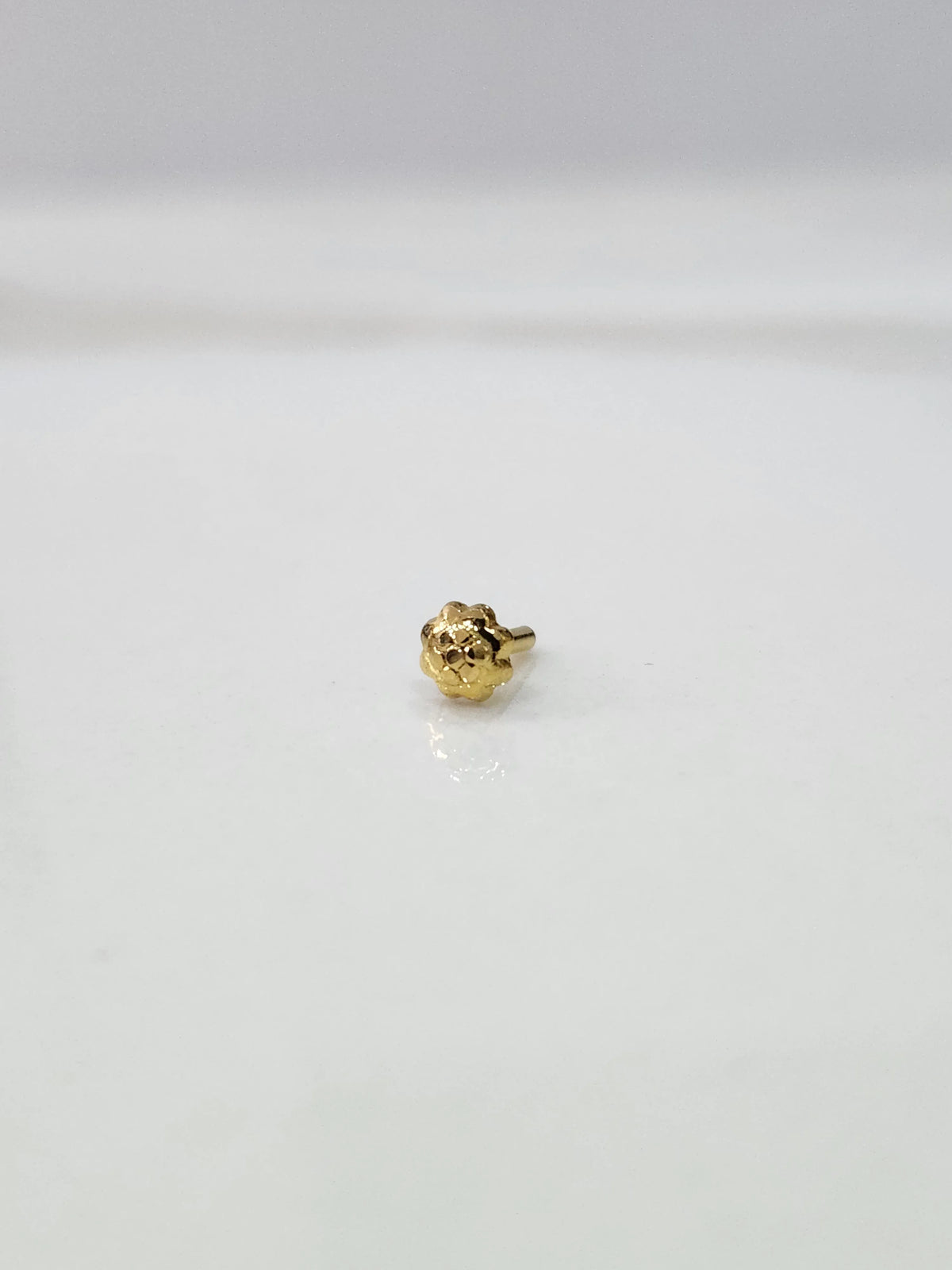 Front view of a small gold nose pin placed on a white background highlighting delicate detailing
