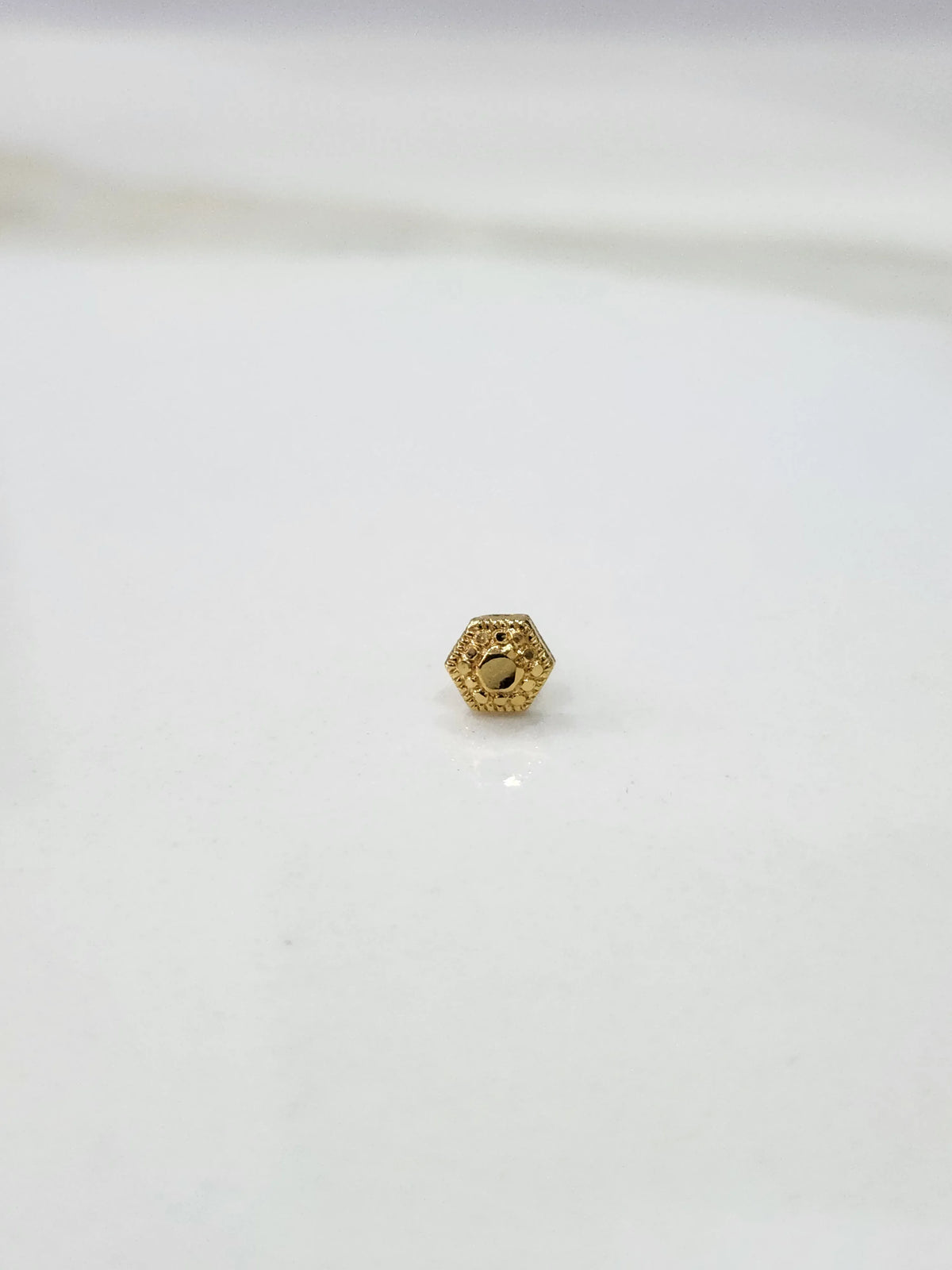 Close-up of tiny 18K Nose Pin Gold on marble surface displaying delicate detailing