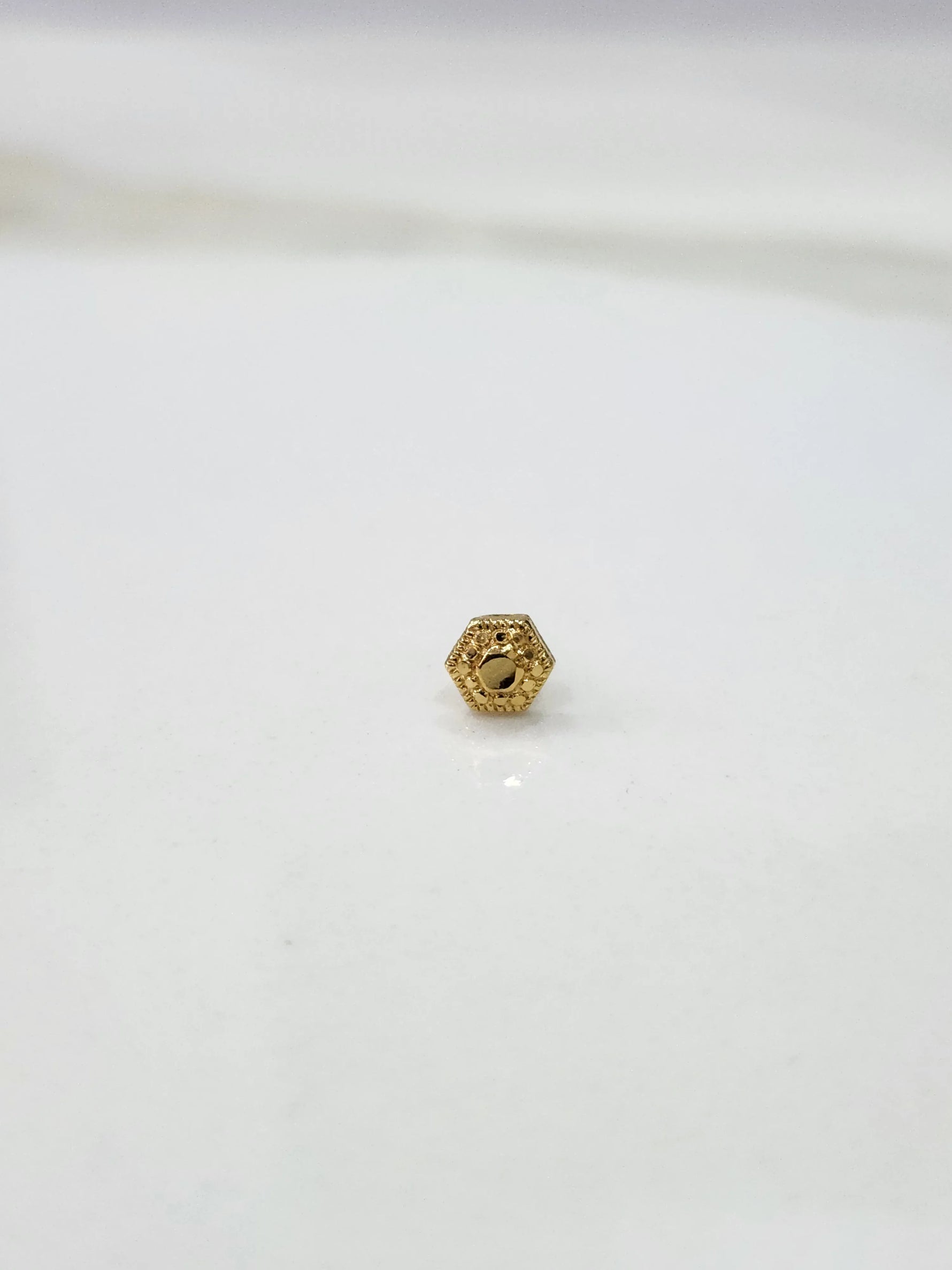Close-up of tiny 18K Nose Pin Gold on marble surface displaying delicate detailing
