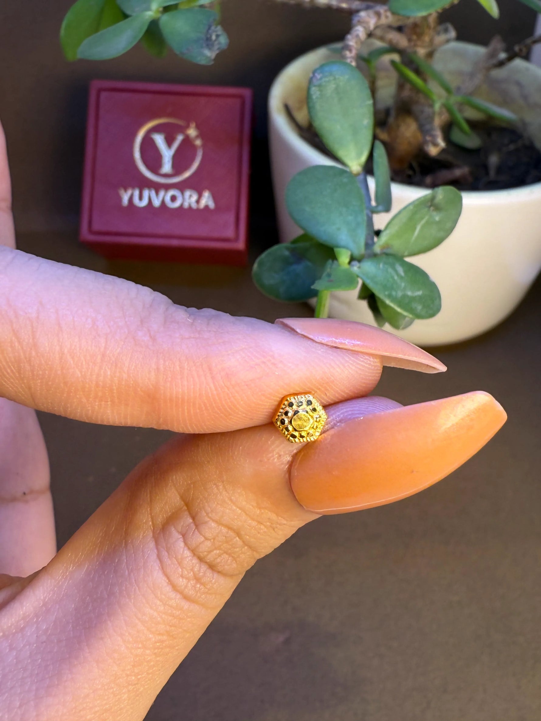 Hand holding tiny 18K Nose Pin Gold beside Yuvora packaging highlighting its small size