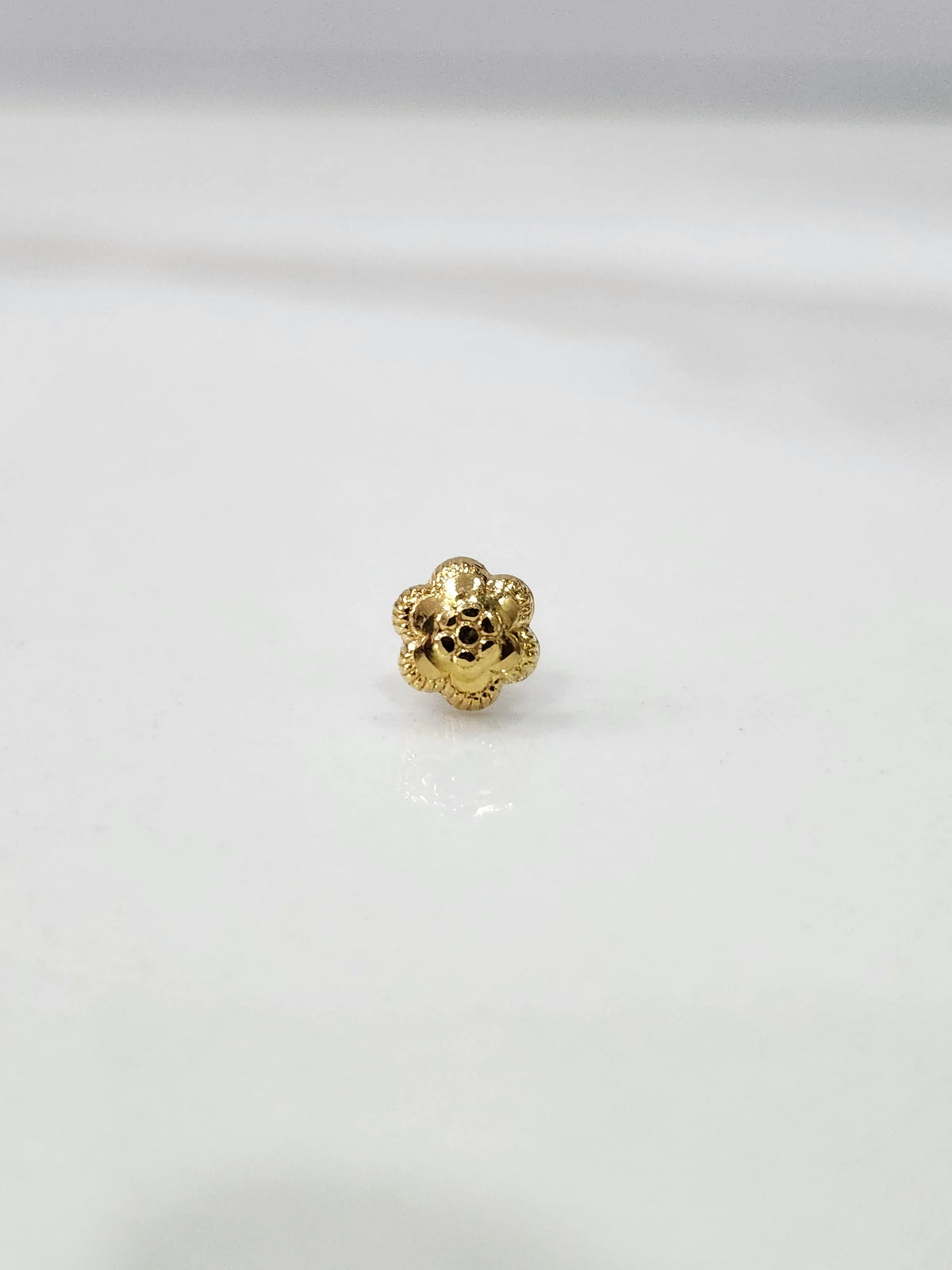 Slight angled close up of a delicate gold nose pin on a white surface showing fine detailing and compact size